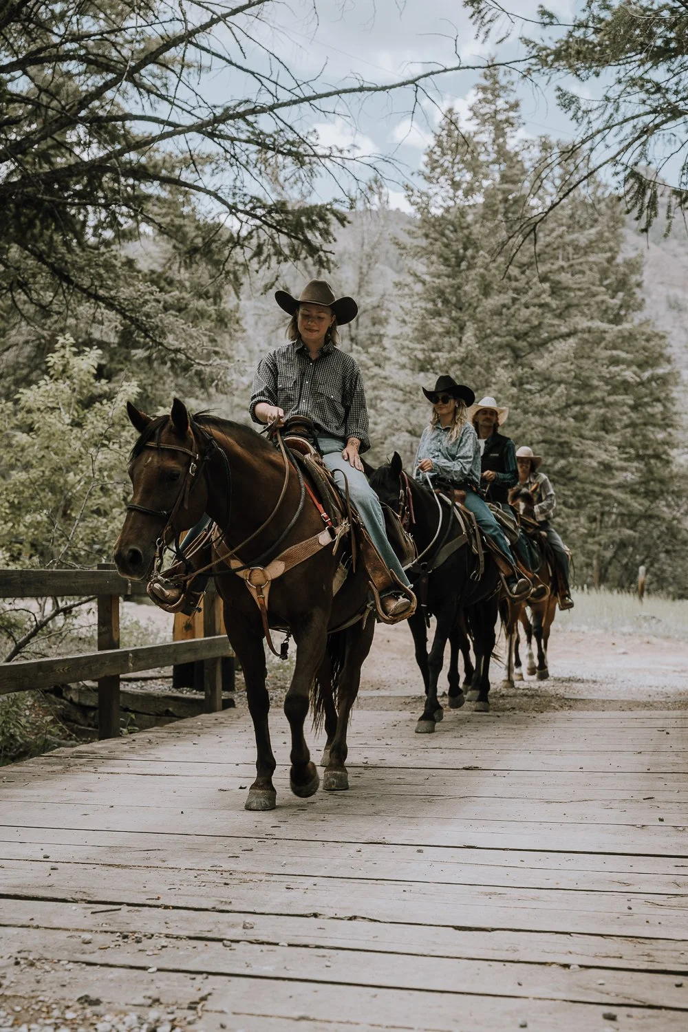 A group of horseback riders cross a bridge during a Wyoming dude ranch vacation.