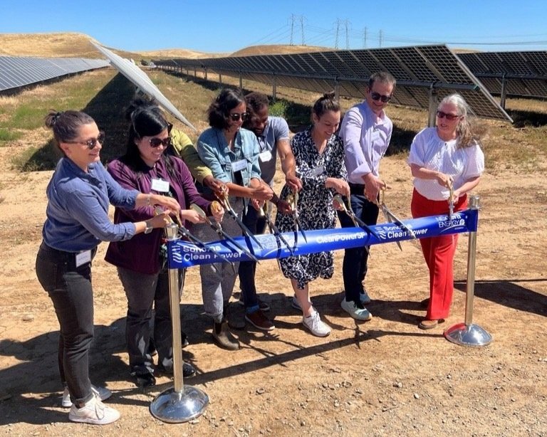 Group of people participating in an outdoor ribbon‑cutting ceremony at a solar facility.