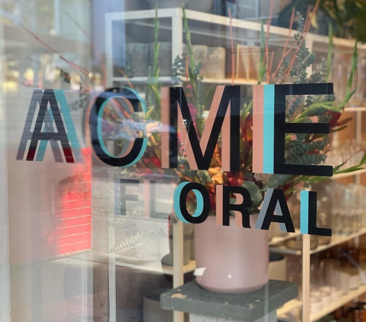 Storefront window showing the text “ACME Floral” with flowers visible behind the glass.