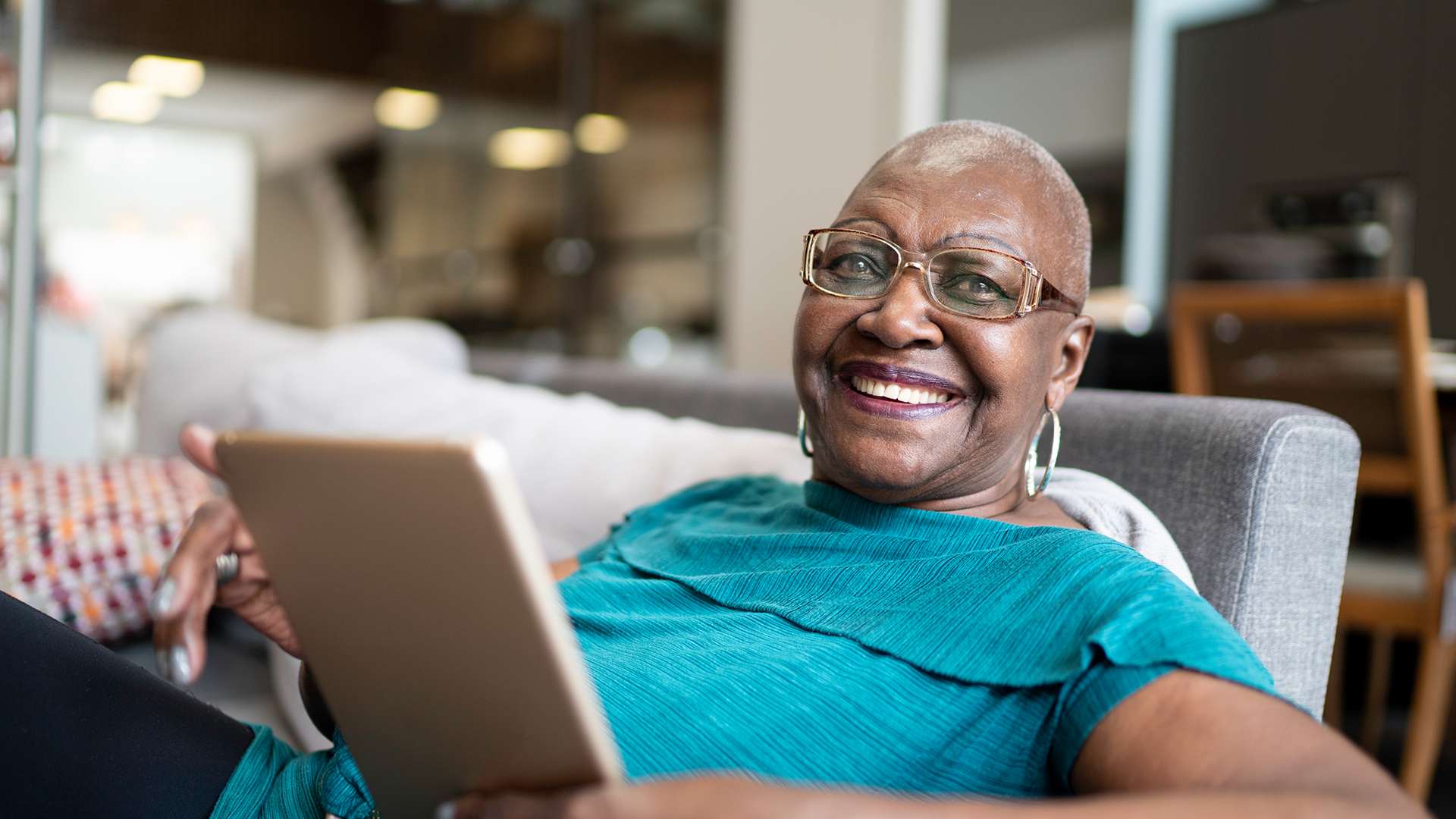 Person relaxing on a couch while holding and viewing a tablet.