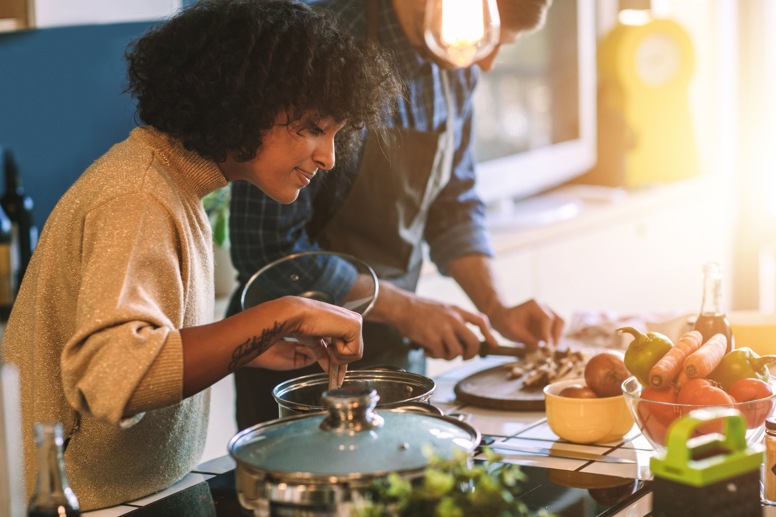People cooking in the kitchen, with one person stirring a pot and another chopping food.