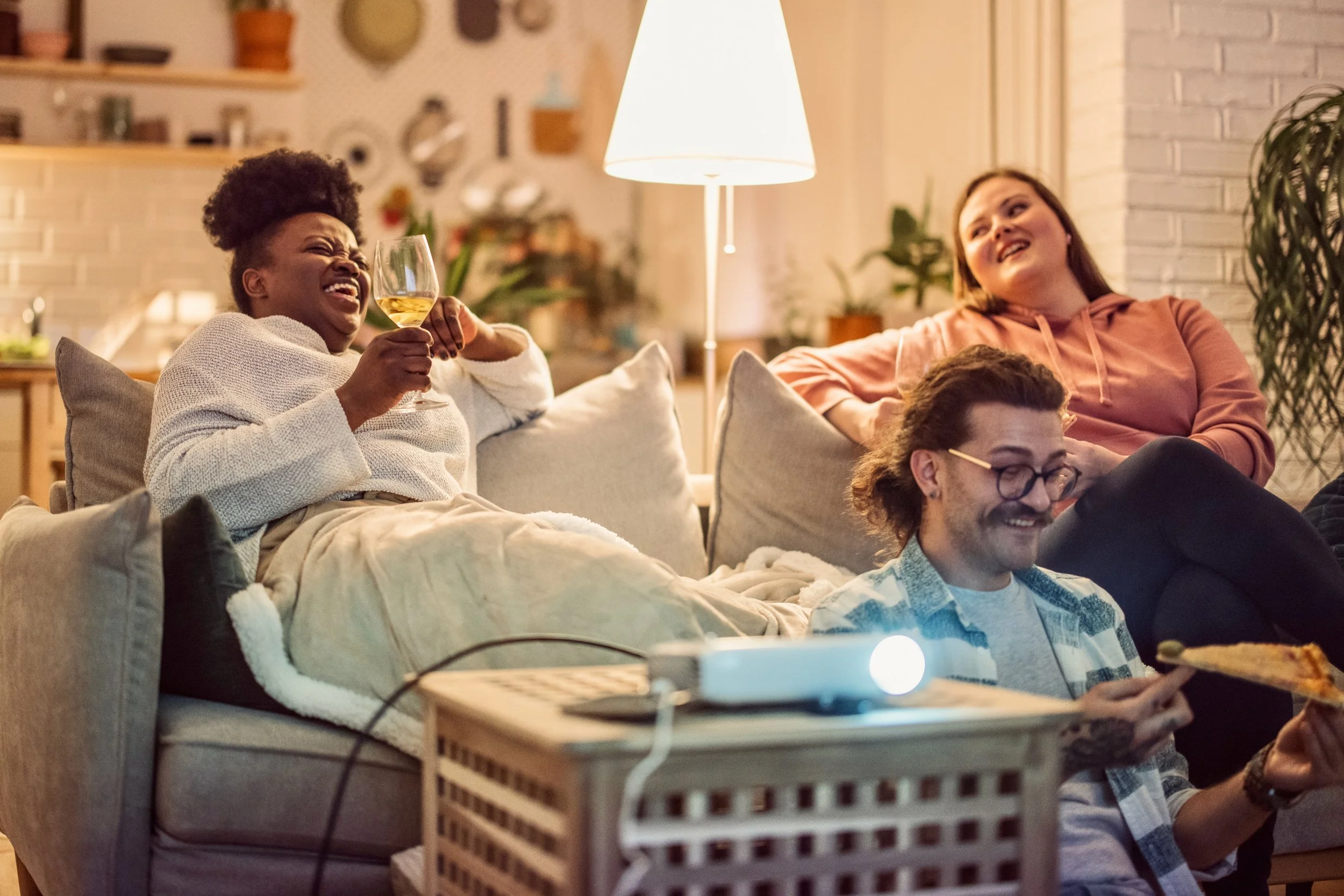 Three people relax on a couch, laughing and watching a movie at home.