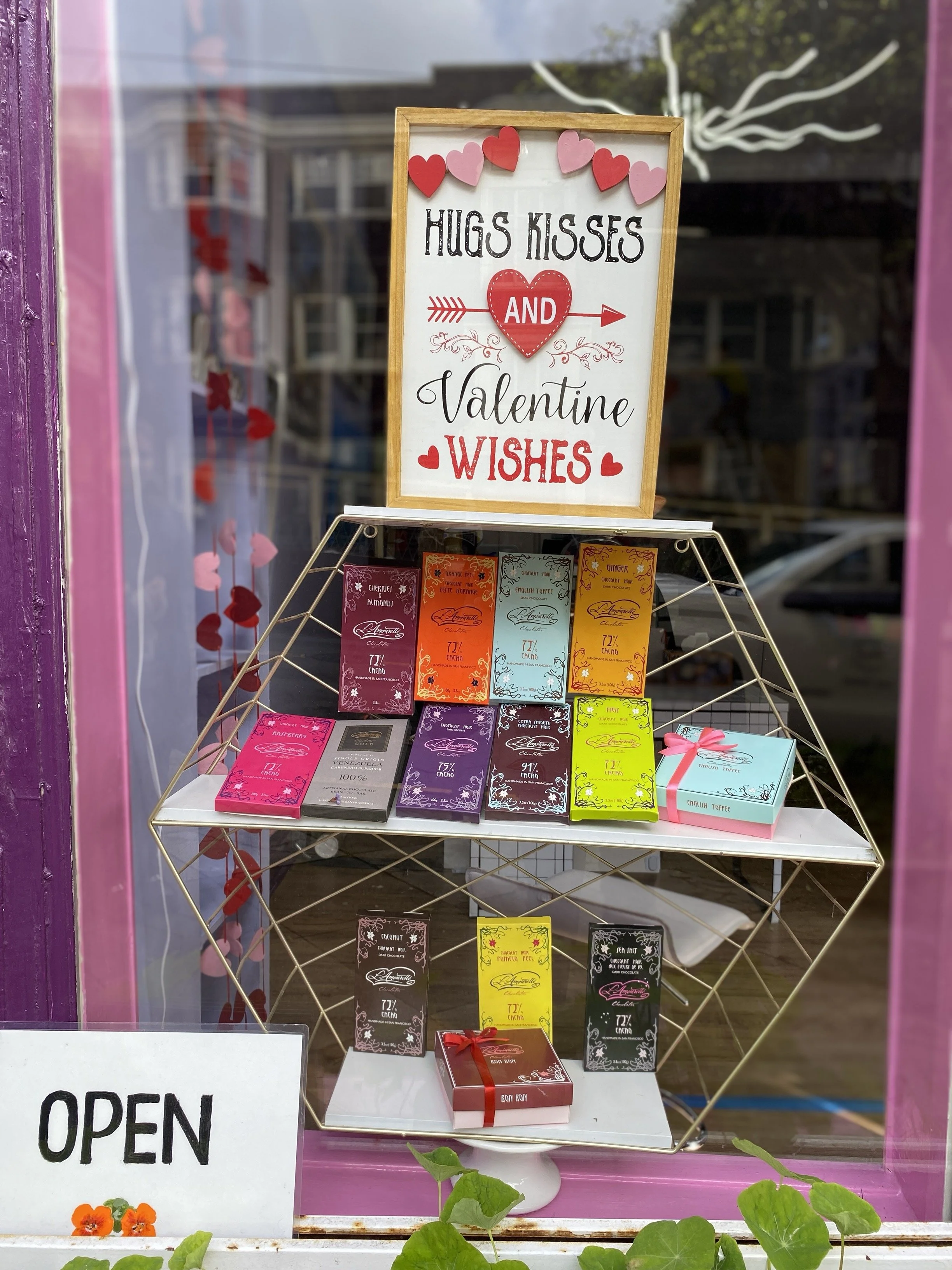 Store window display featuring Valentine‑themed signage and shelves of boxed chocolates.