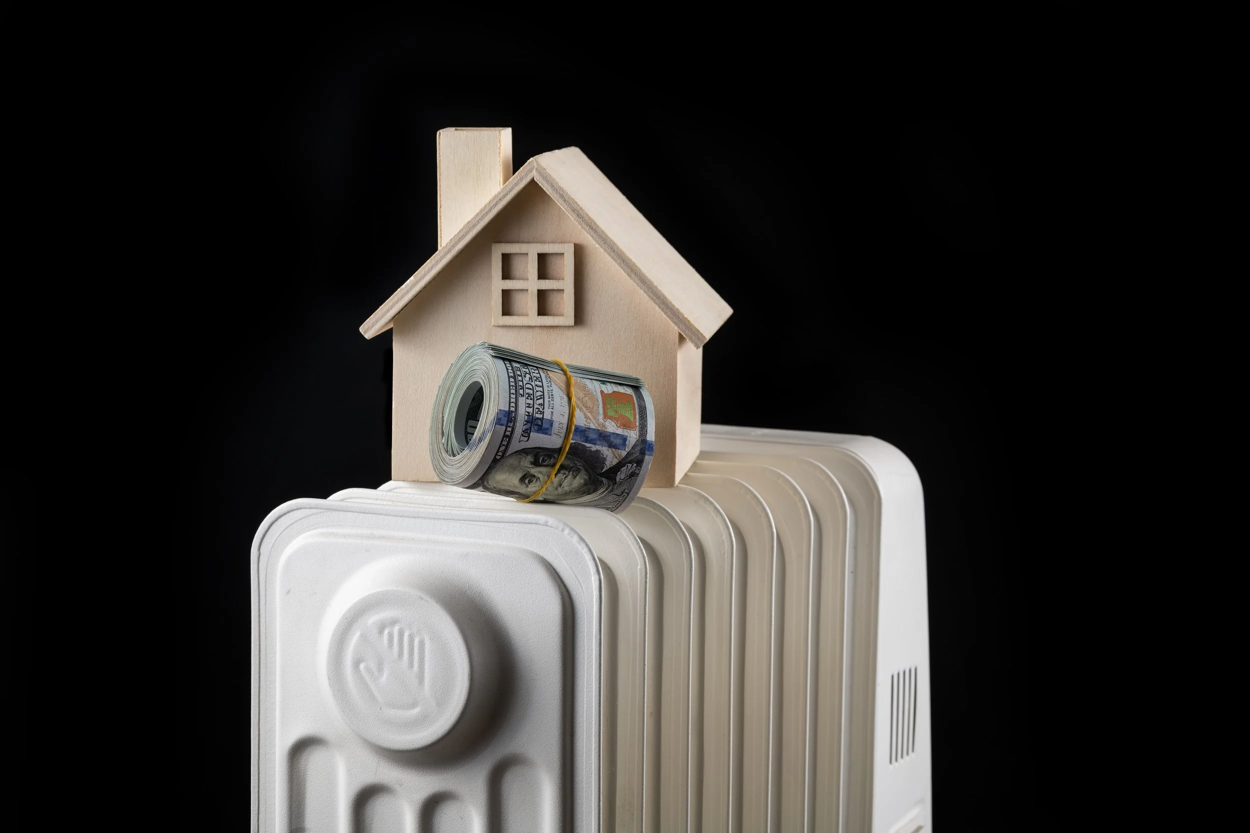 Small model house and rolled currency placed on top of a home radiator.
