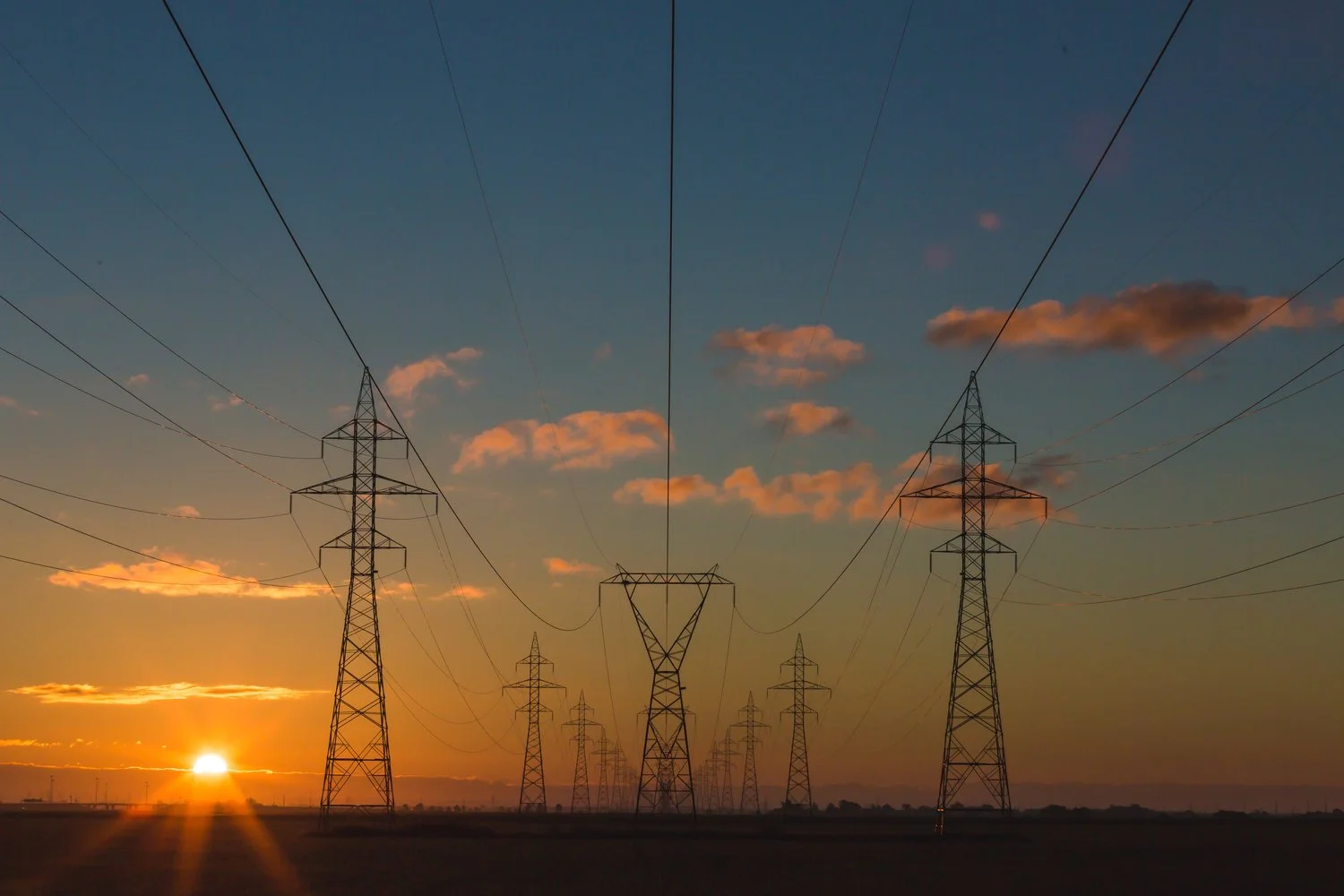 Power transmission towers and lines silhouetted against a sunset sky.