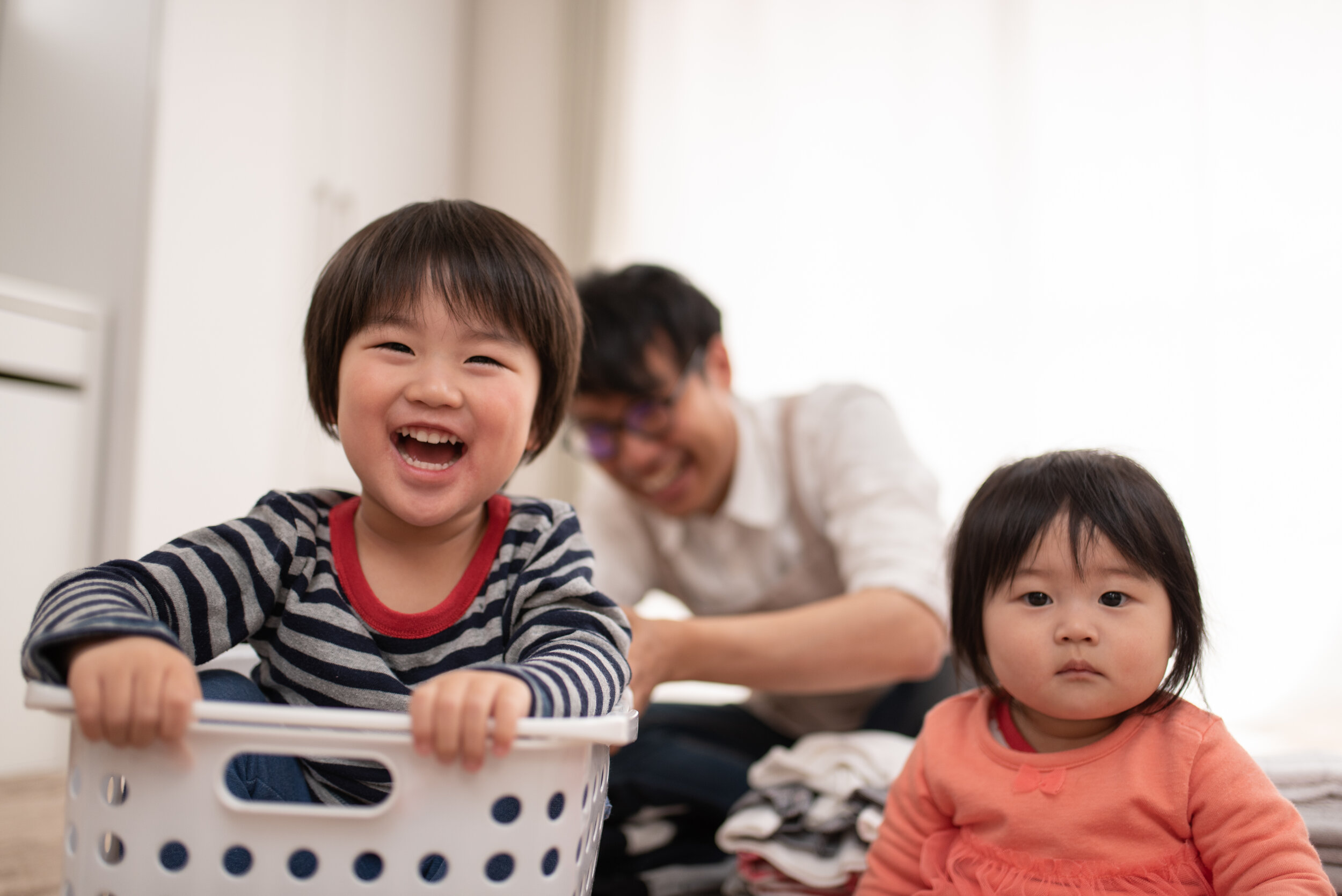 Two children smiling and playing with their parent behind them.