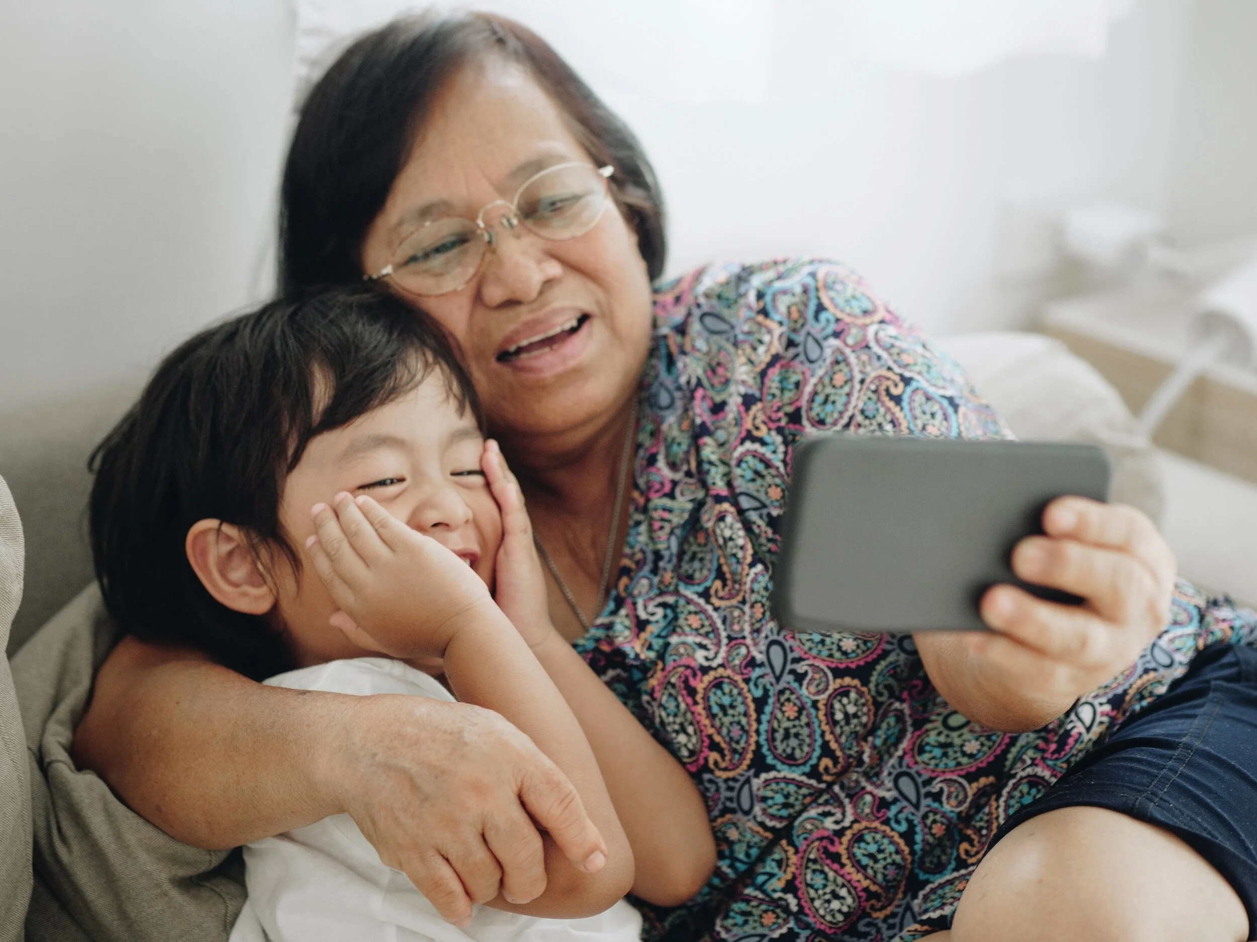 A person and their grandparent looking at a device and smiling.