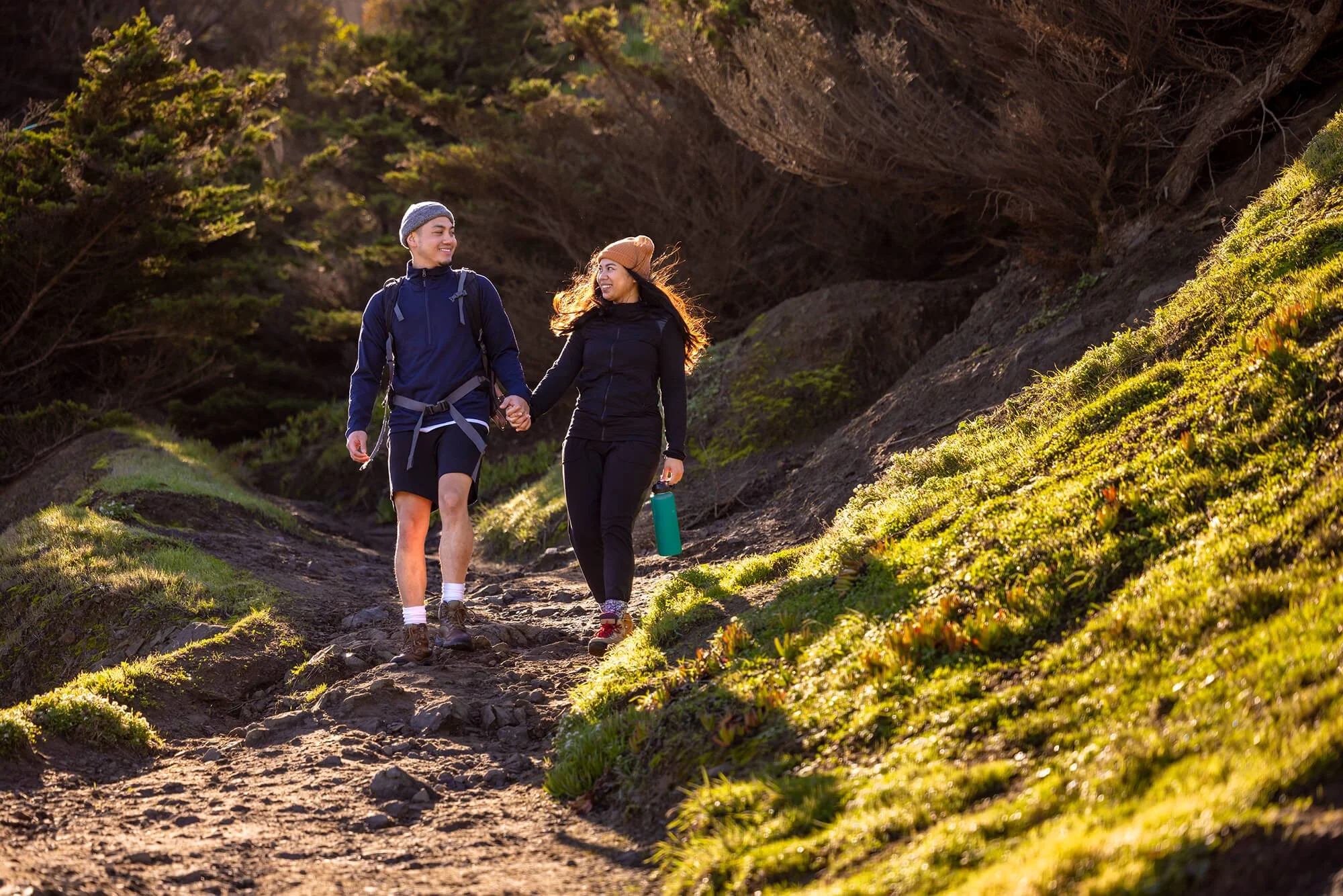 A couple holding hands and walking in a grassy area.