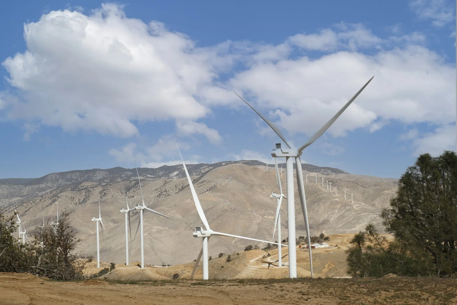 Multiple wind turbines along dry hills.