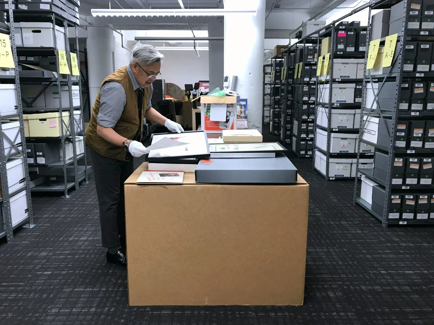 Archivist handling framed artwork in a storage room with labeled boxes.