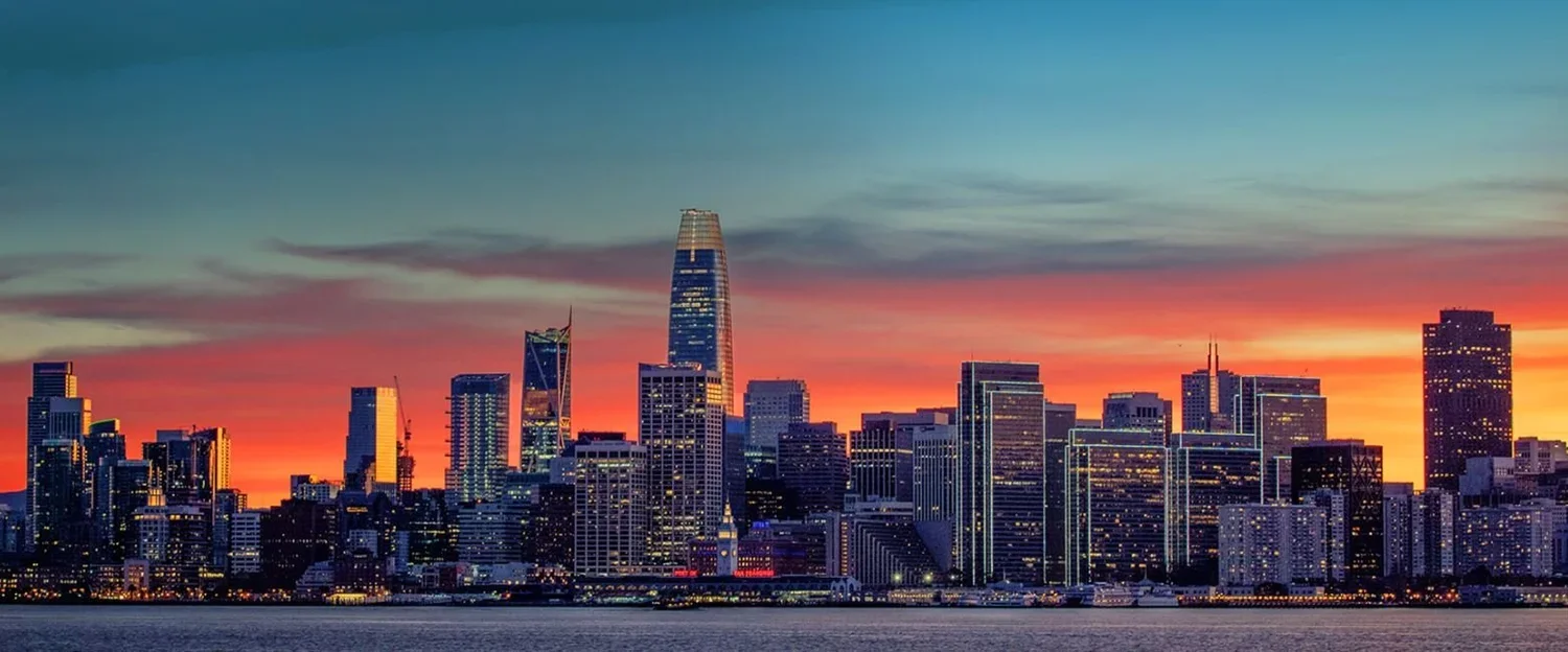 San Francisco skyline at sunset with illuminated skyscrapers.