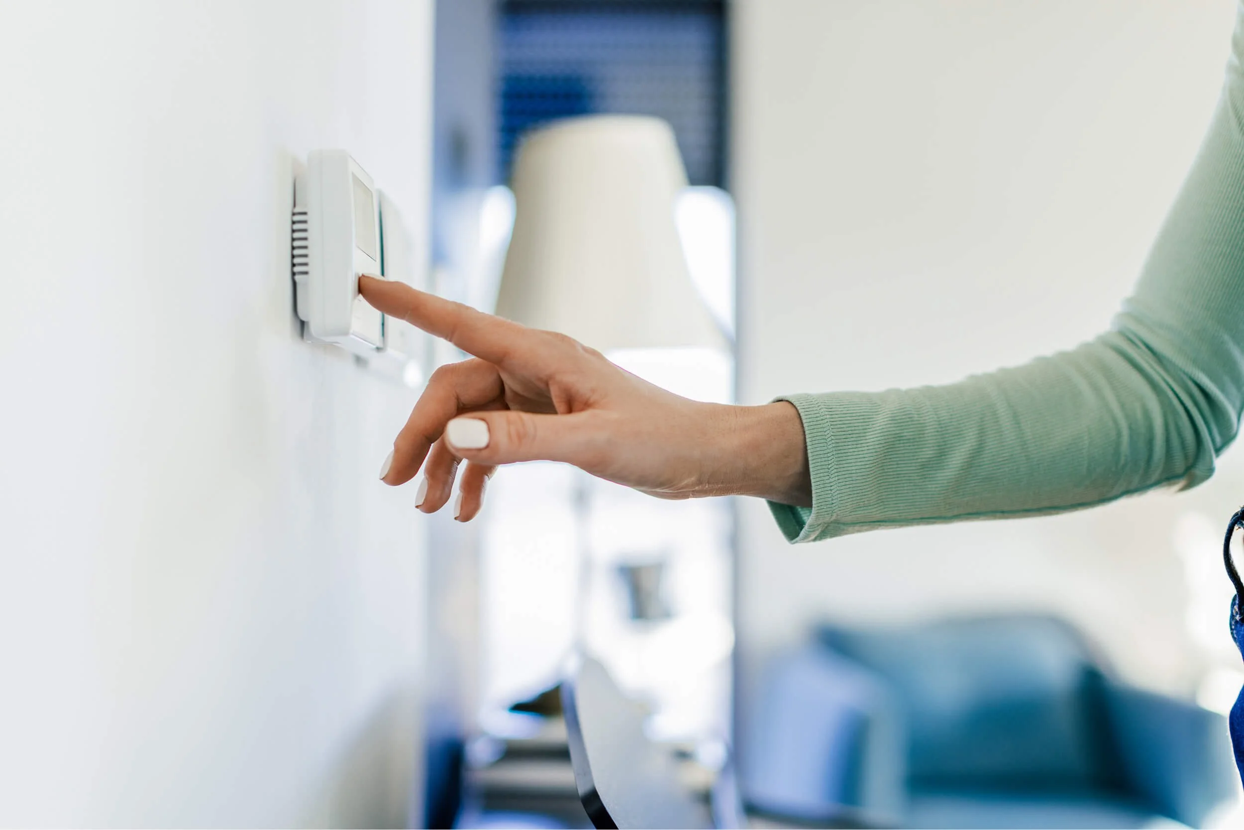 A person adjusting the thermostat on the wall.