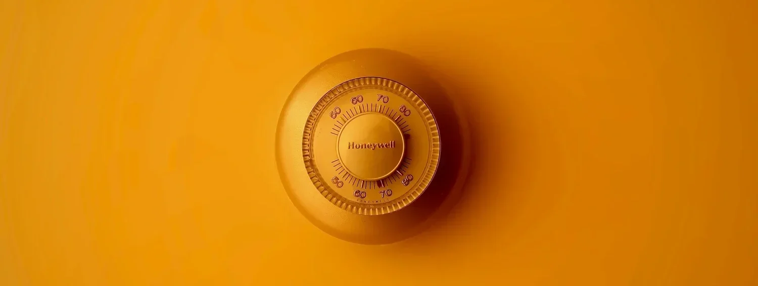 Round thermostat on an orange wall.