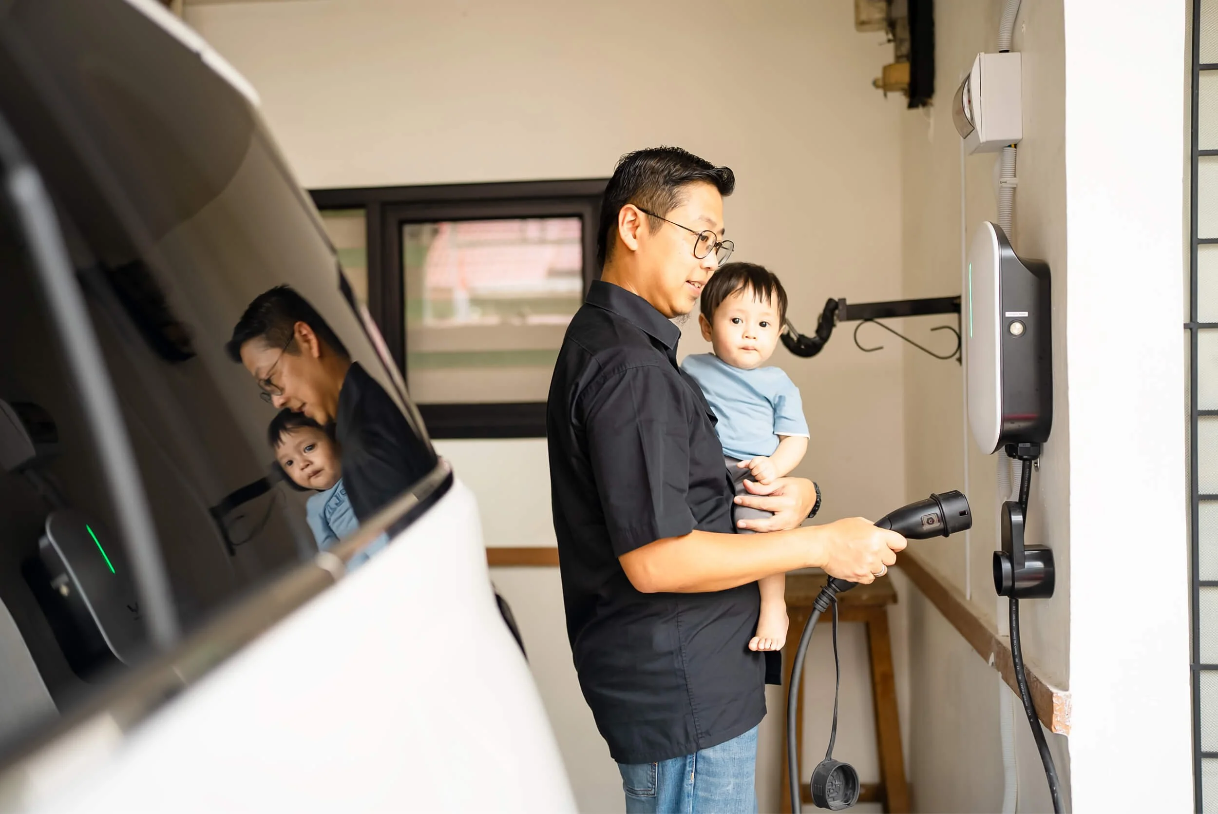 A parent holding their child while holding an electric vehicle charger in a different hand.