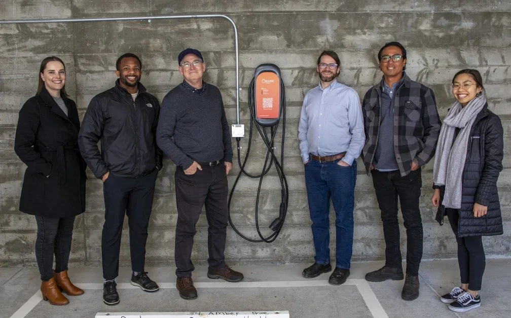 Group of people standing beside an electric vehicle charging station.
