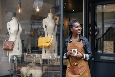Shop owner smiling in a storefront with mannequins displaying handbags.