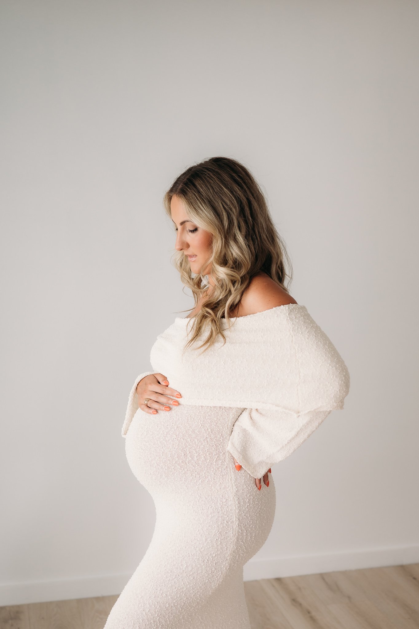 pregnant mother in white knit dress cradling bump during studio maternity session Houston TX