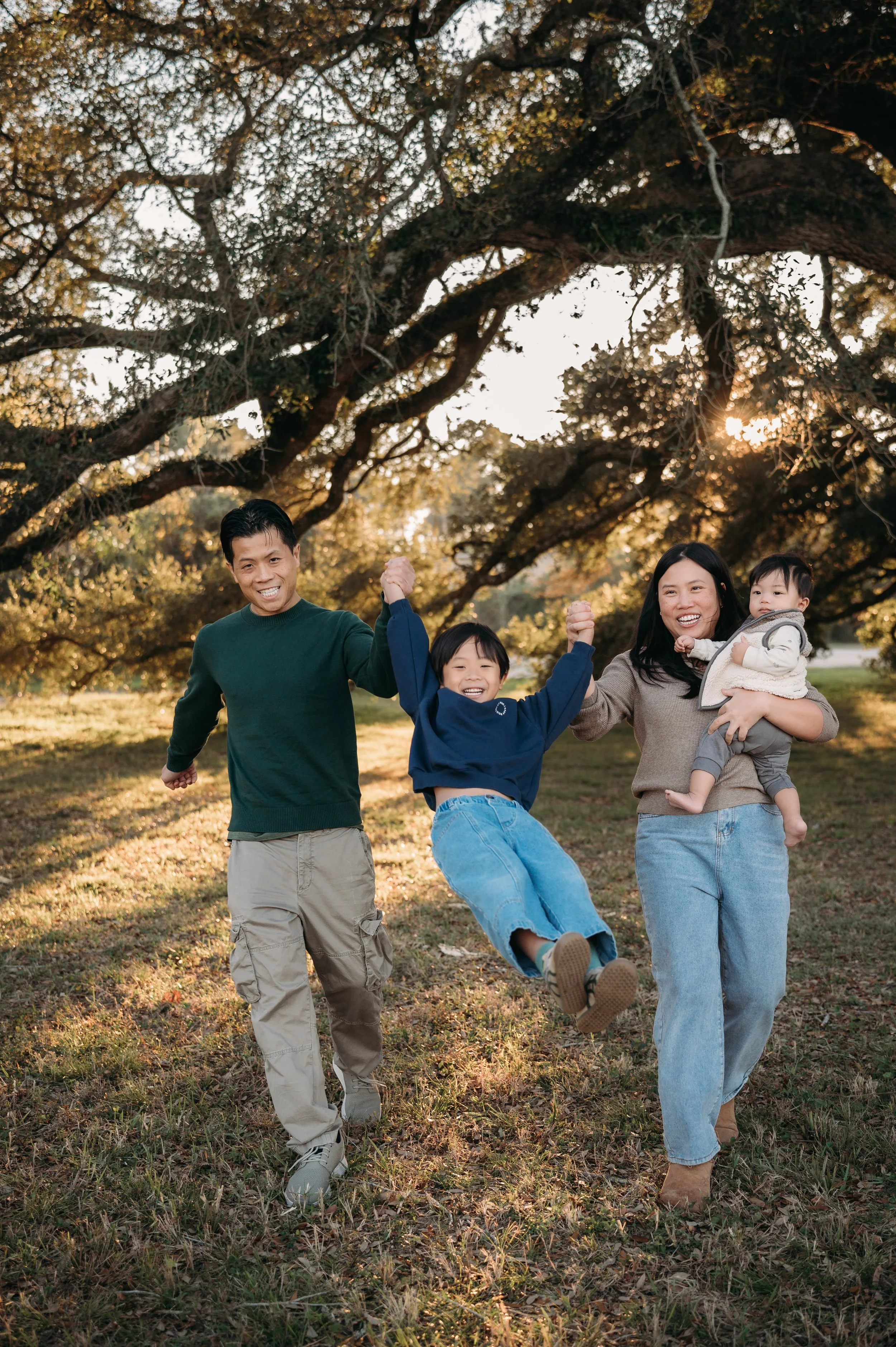 family of four running and laughing under oak tree during outdoor family session Houston TX