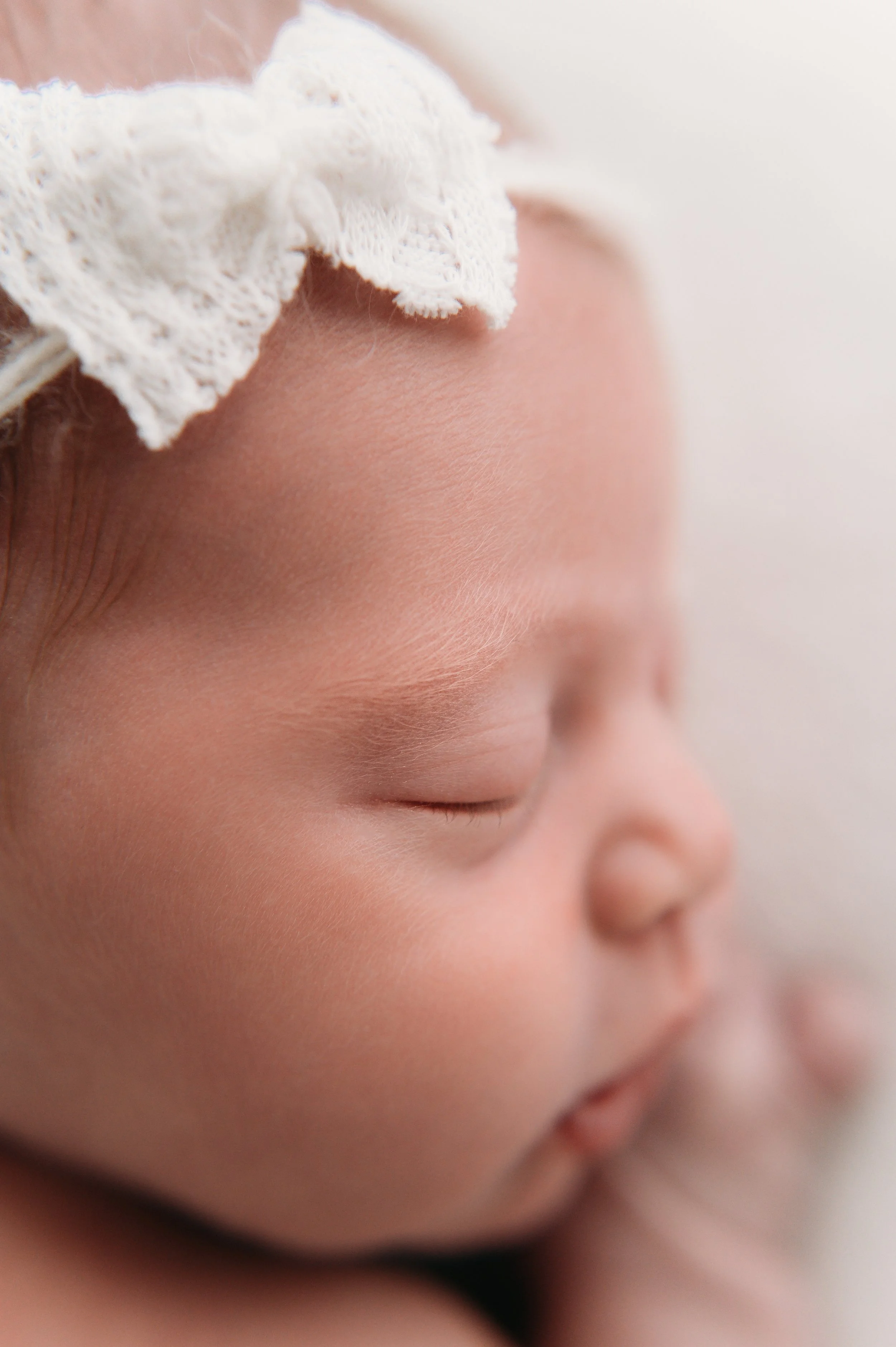 close up of sleeping newborn baby face with lace bow headband during studio session The Woodlands TX