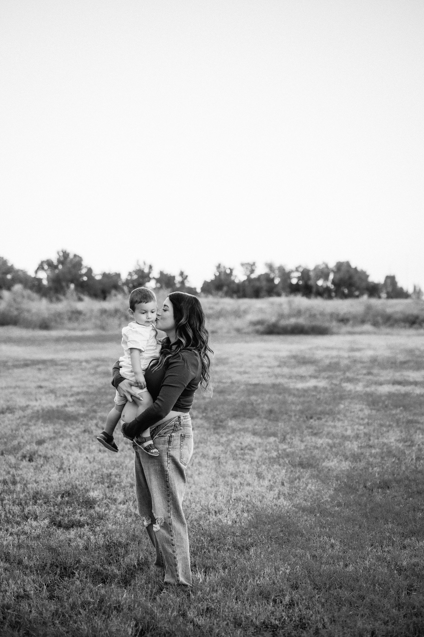 black and white photo of pregnant mother holding toddler in open field during outdoor maternity session The Woodlands TX