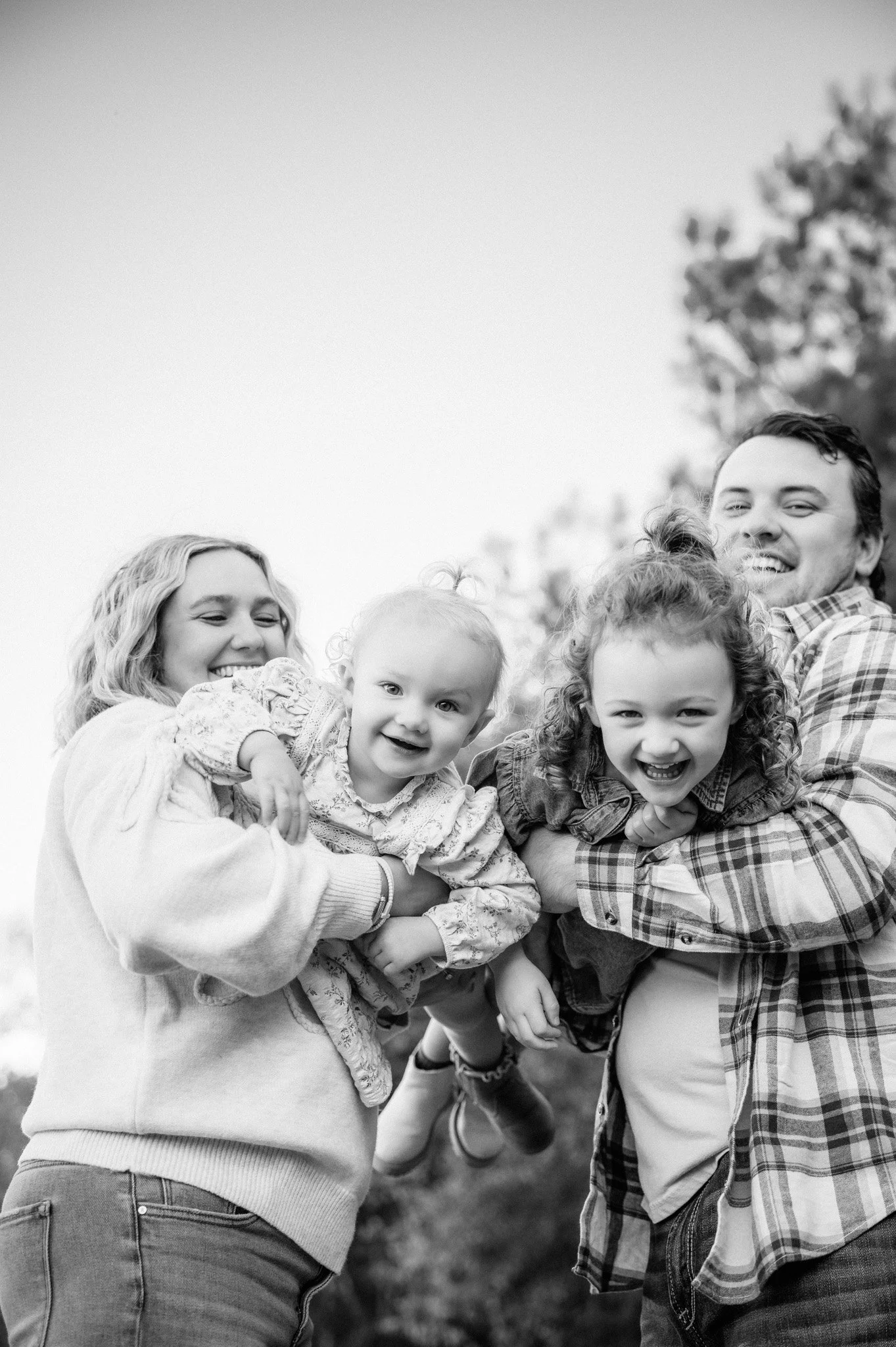 black and white photo of family of four laughing together during outdoor family session Houston TX