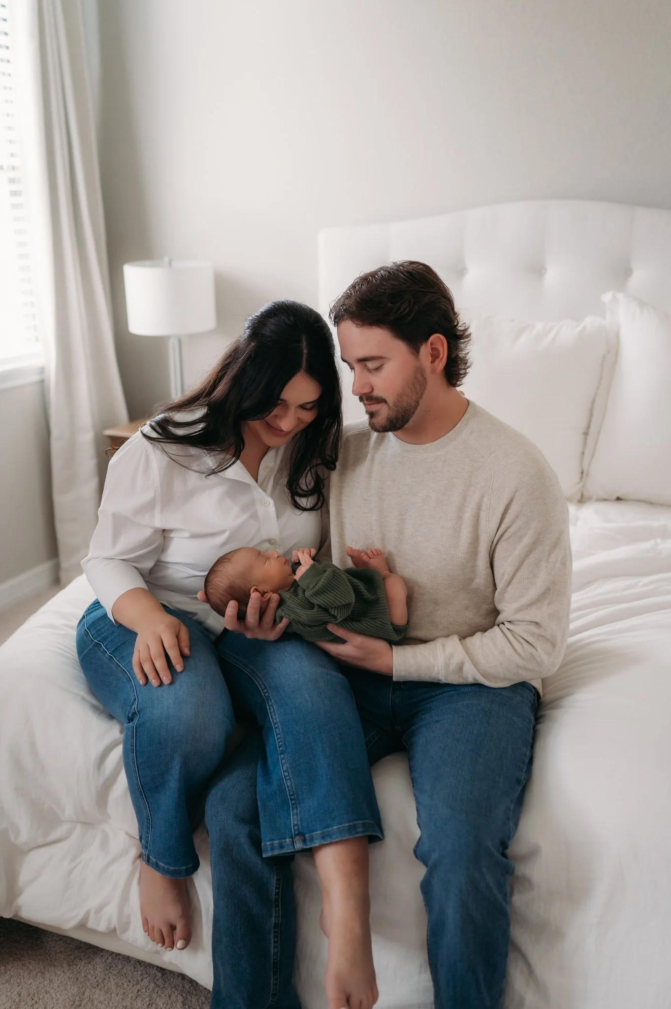 new parents sitting on bed gazing at newborn baby during in-home newborn session Houston TX