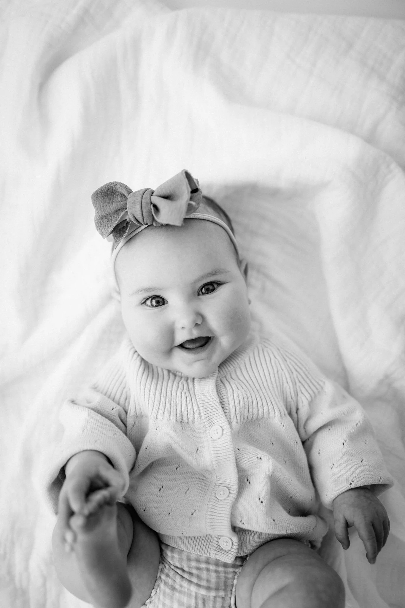 black and white photo of smiling baby girl with bow headband during sitter milestone session Houston TX