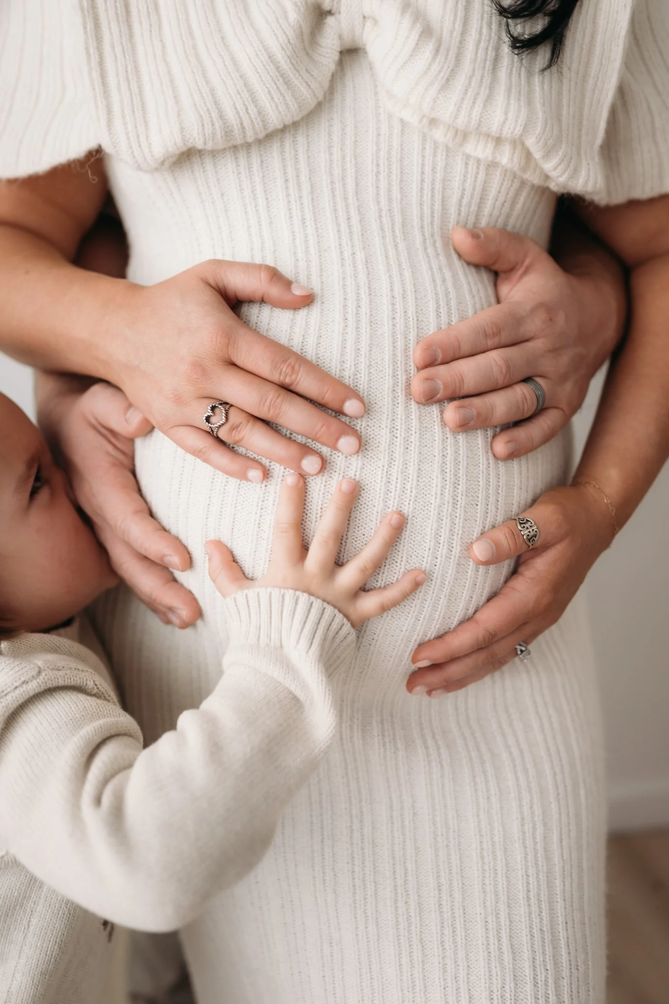 close up of partner's hands cradling pregnant belly in white knit dress during maternity session Houston TX