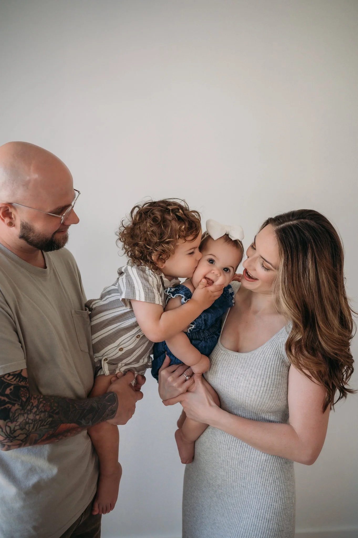 father and mother smiling at toddler kissing baby sibling during studio family session Houston TX