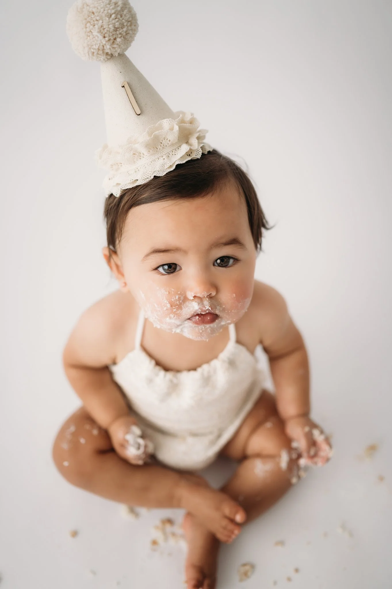 baby girl in party hat with cake on face during first birthday cake smash session Houston TX