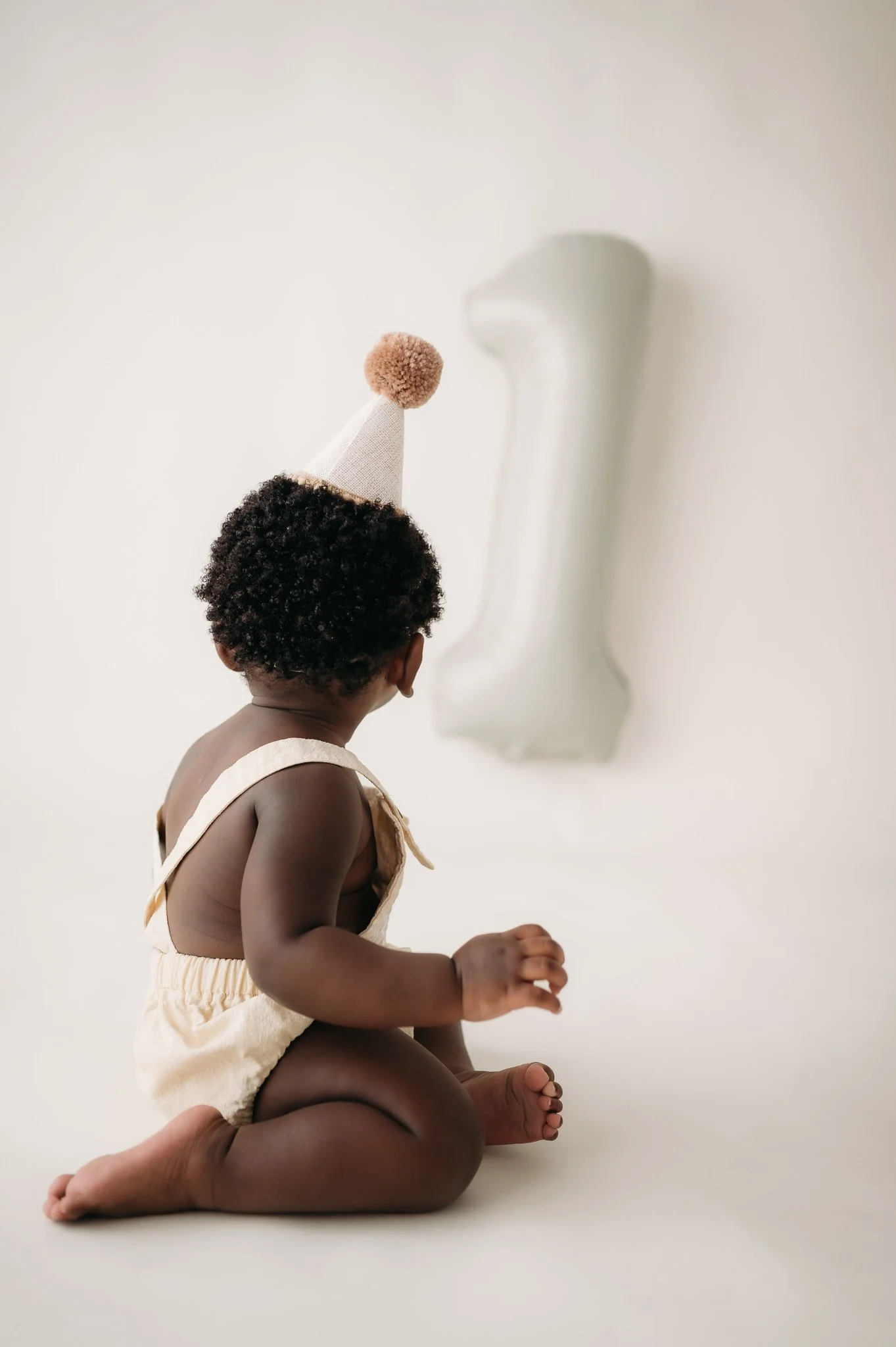 baby in party hat looking up during first birthday milestone session Houston TX
