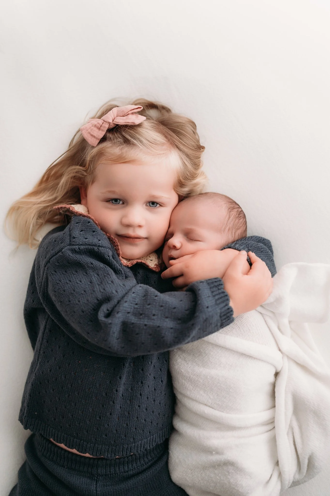 toddler girl hugging and smiling at sleeping newborn sibling during studio newborn session Houston TX