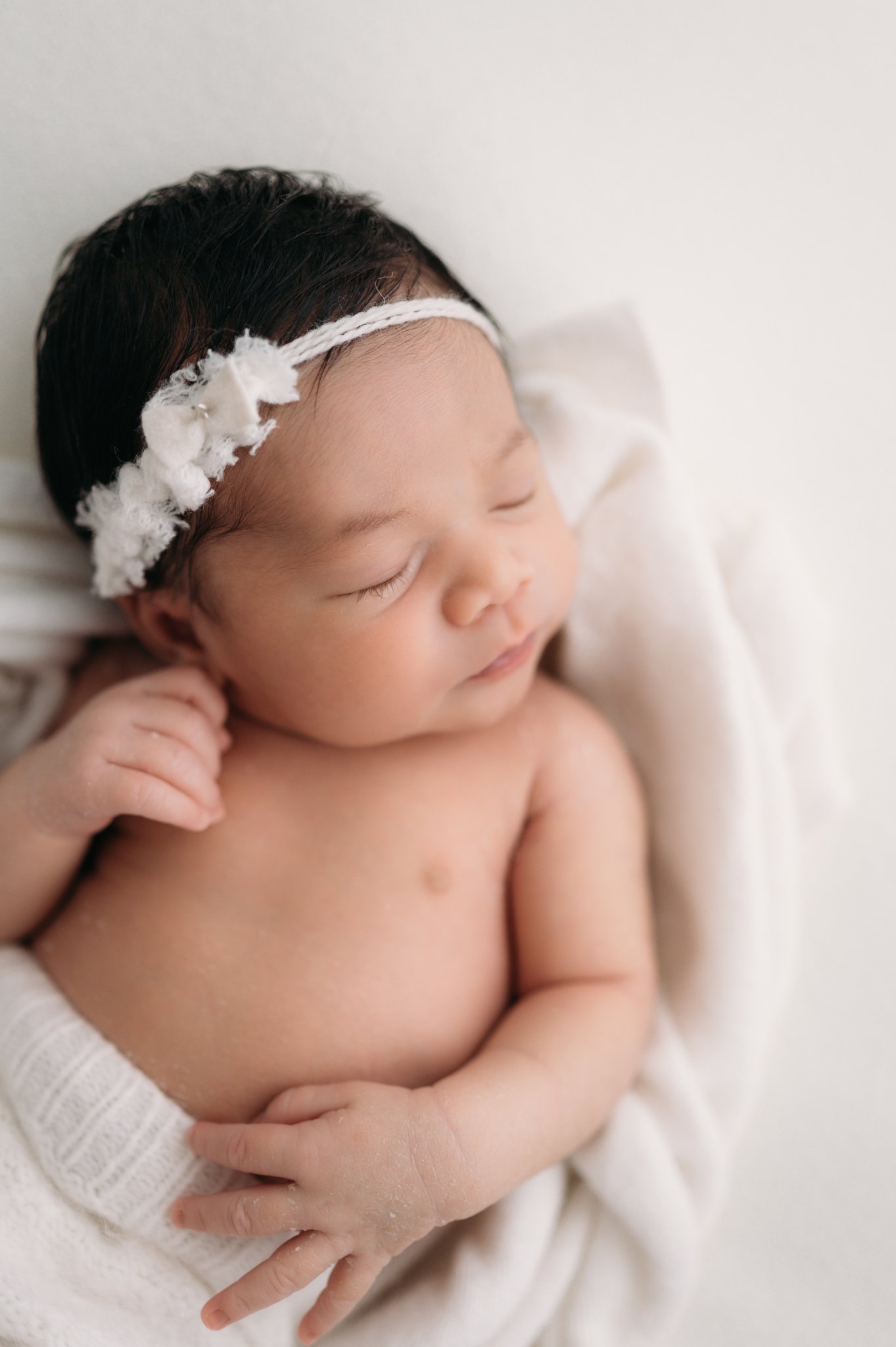 sleeping newborn baby girl with white headband on cream blanket during studio newborn session Houston TX