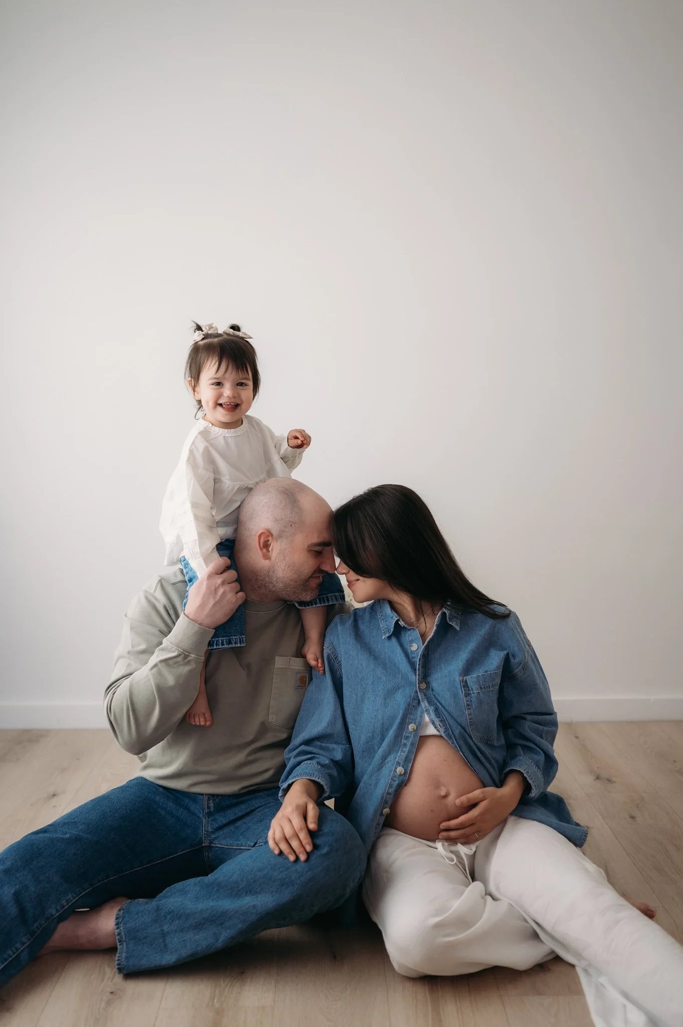 pregnant mother and father sitting on floor with toddler on shoulders during maternity session Houston TX