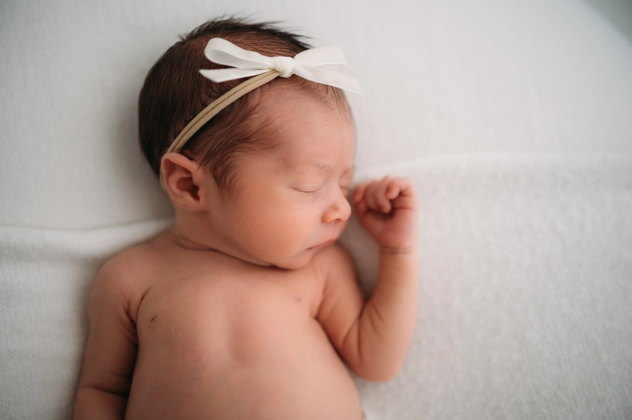 sleeping newborn baby with white bow headband during studio newborn session The Woodlands TX