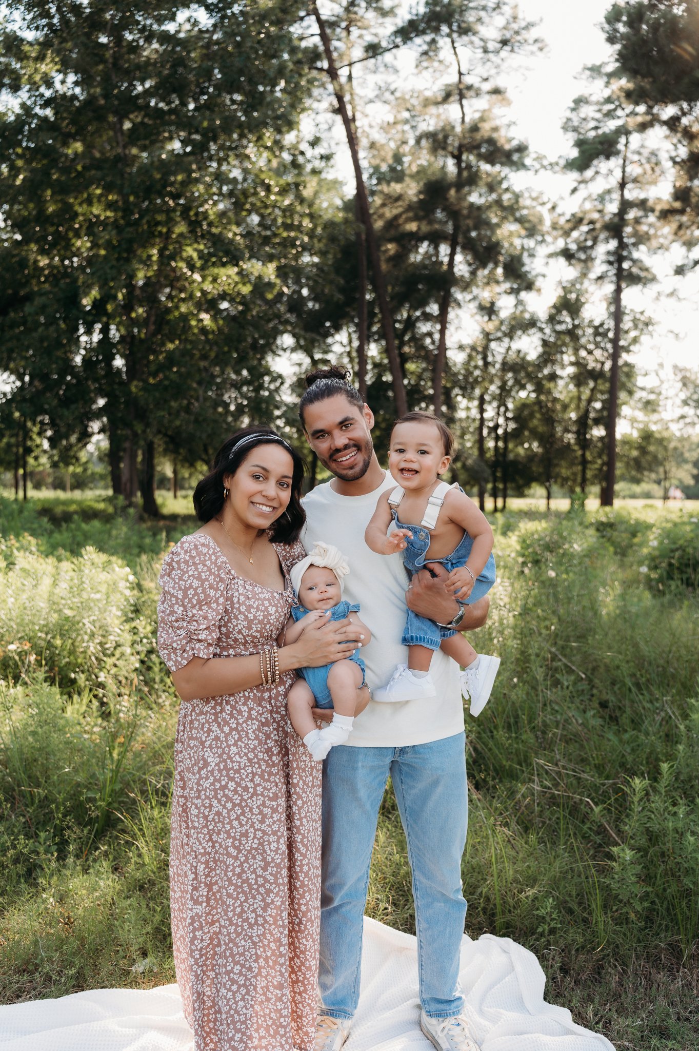 family of four standing together in wooded park during outdoor family session Houston TX
