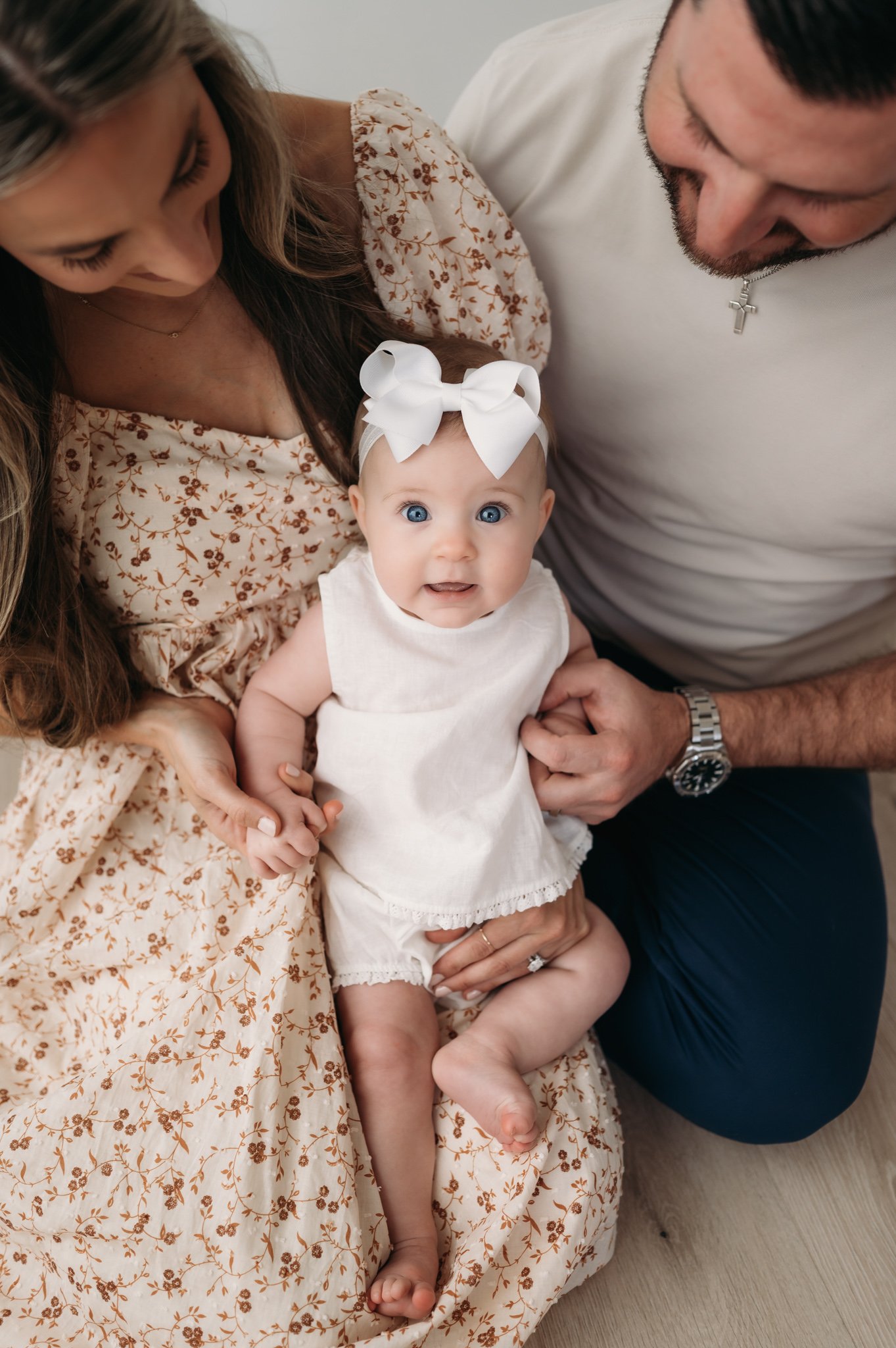 parents gazing down at baby girl with bow during studio family session The Woodlands TX