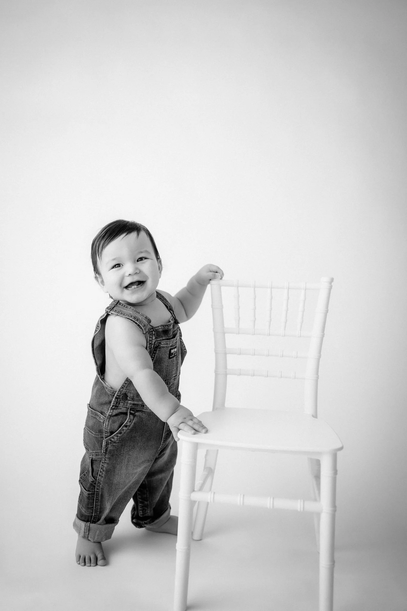 Smiling baby standing and holding a chair during a milestone photography session at a Woodlands baby photography studio