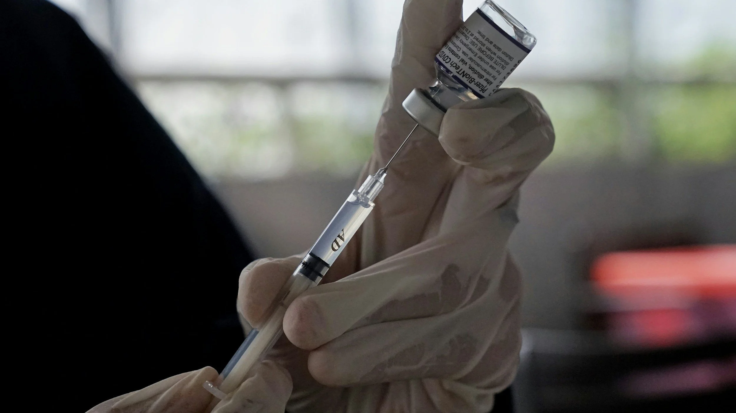 Person wearing gloves drawing liquid from a vial into a syringe.