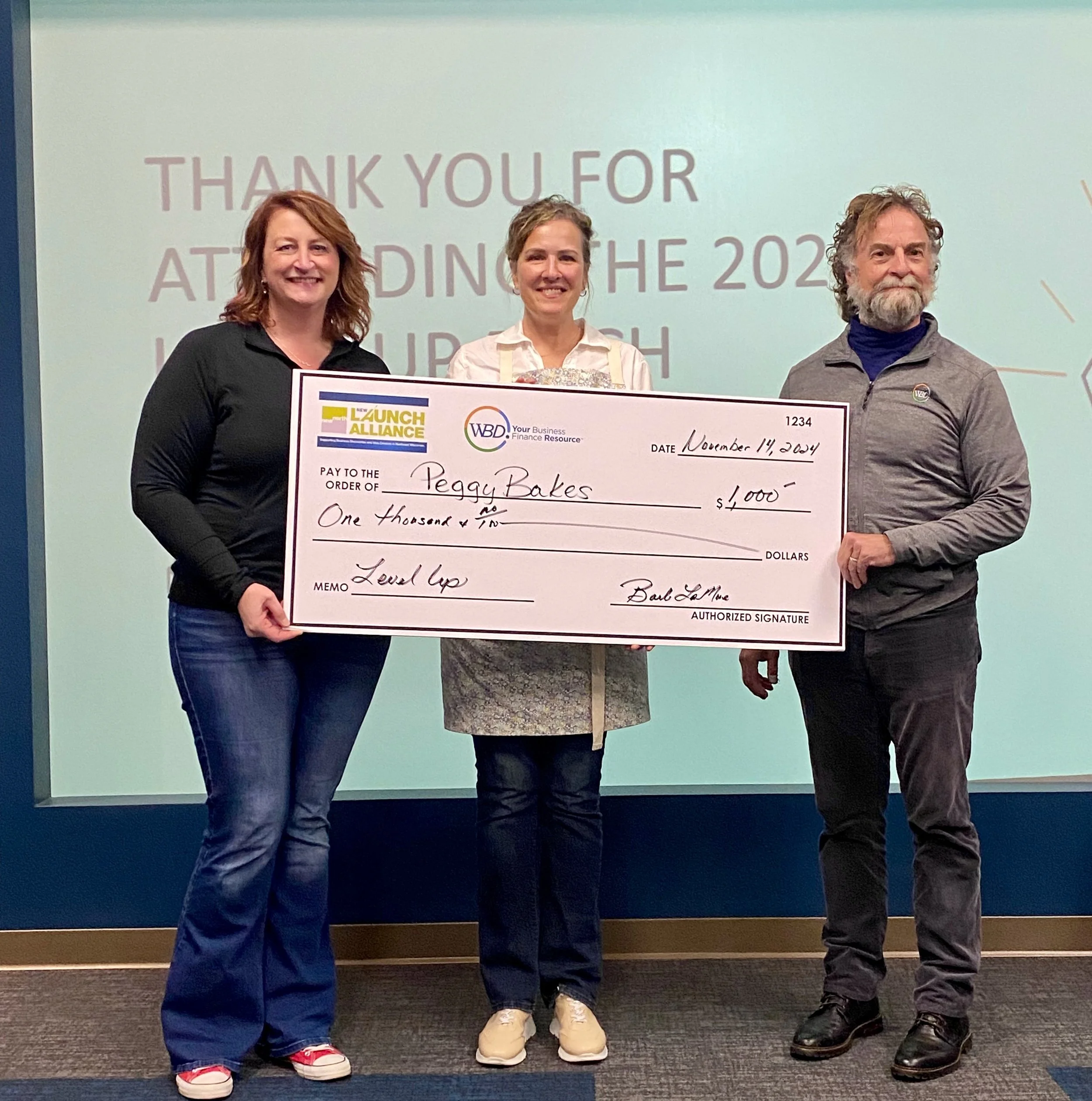 Peggy Bakes founder, Peggy Sonnenburg standing with two other other individuals holding her big check from her first place winning of the New North pitch contest