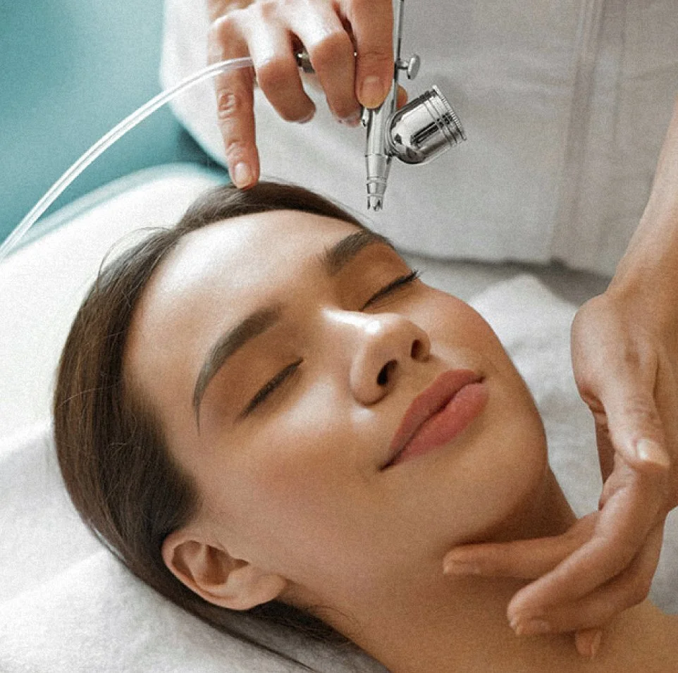 Cosmetologist performing a jet peel facial using an airbrush system on a female client