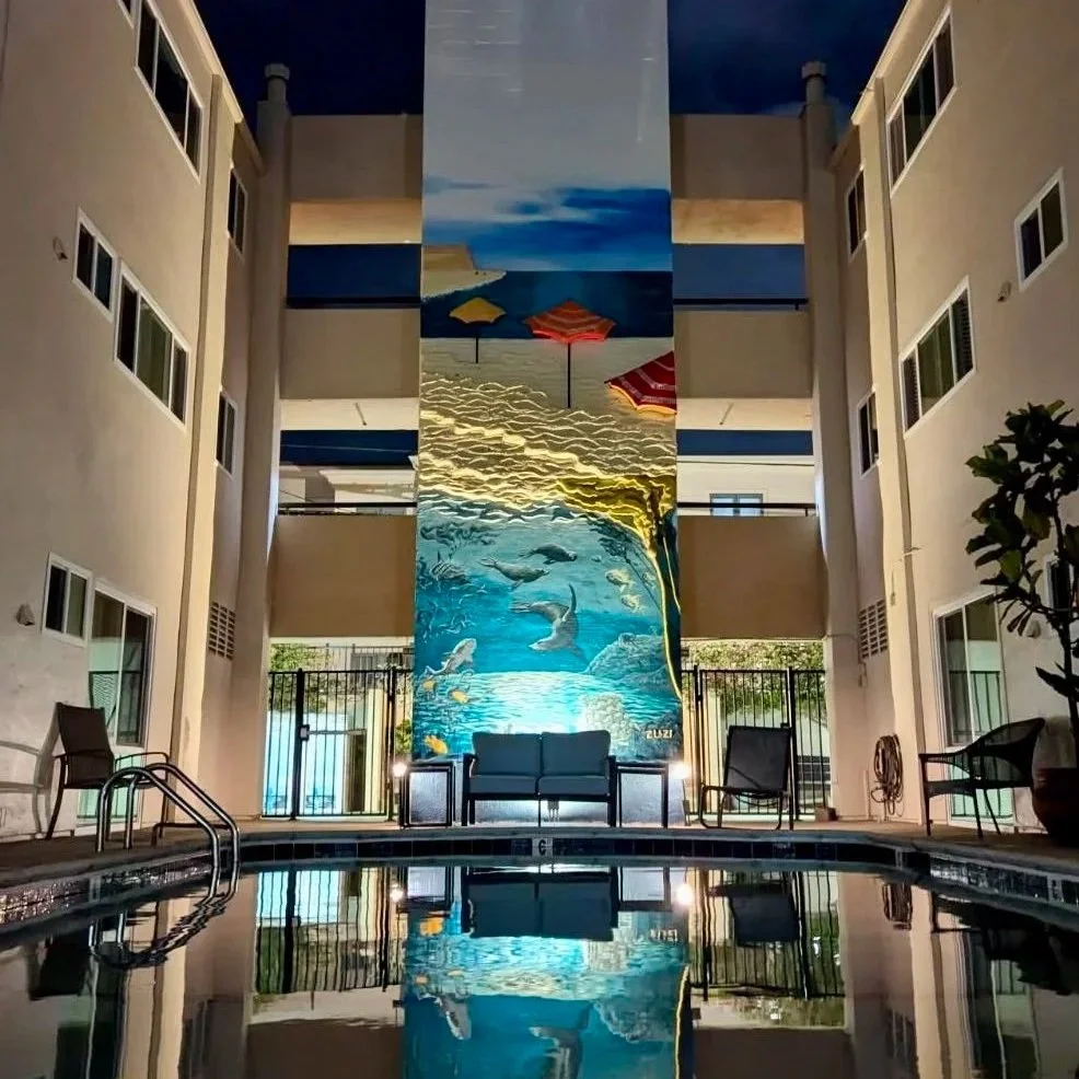 Teeming with Life mural at night, lit up and reflected in the pool at Casa Linda Apartments in La Jolla