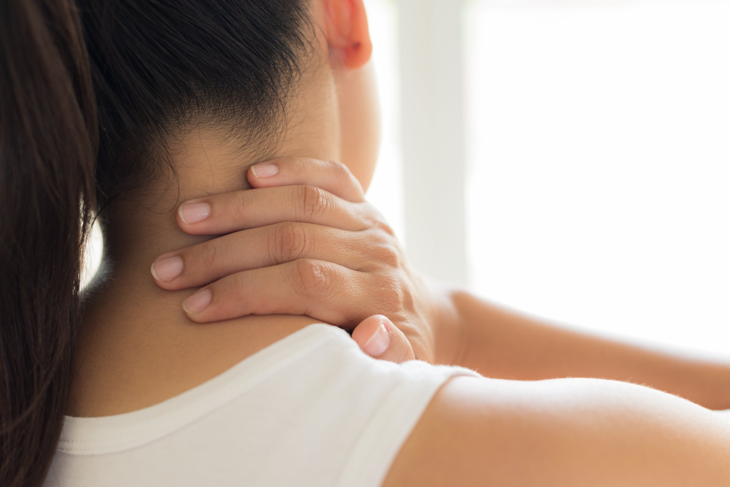 Person holding the back of their neck in pain, representing common neck pain and stiffness symptoms.
