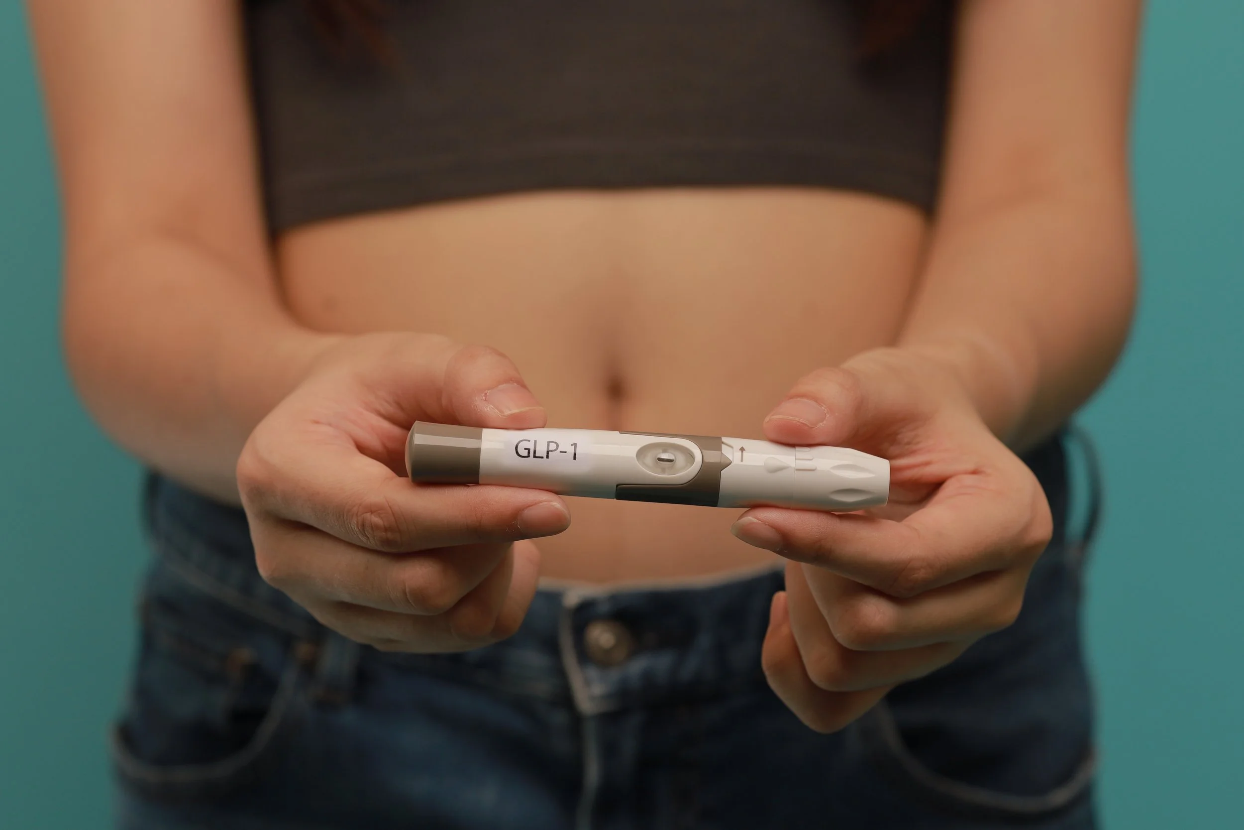 Person holding a GLP-1 injection pen, representing GLP-1 weight loss and strength training support.