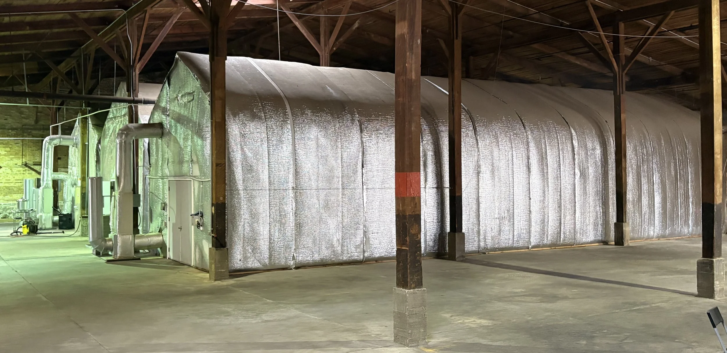 Large industrial air filtration system with silver insulated ducts and wooden support beams inside a warehouse.