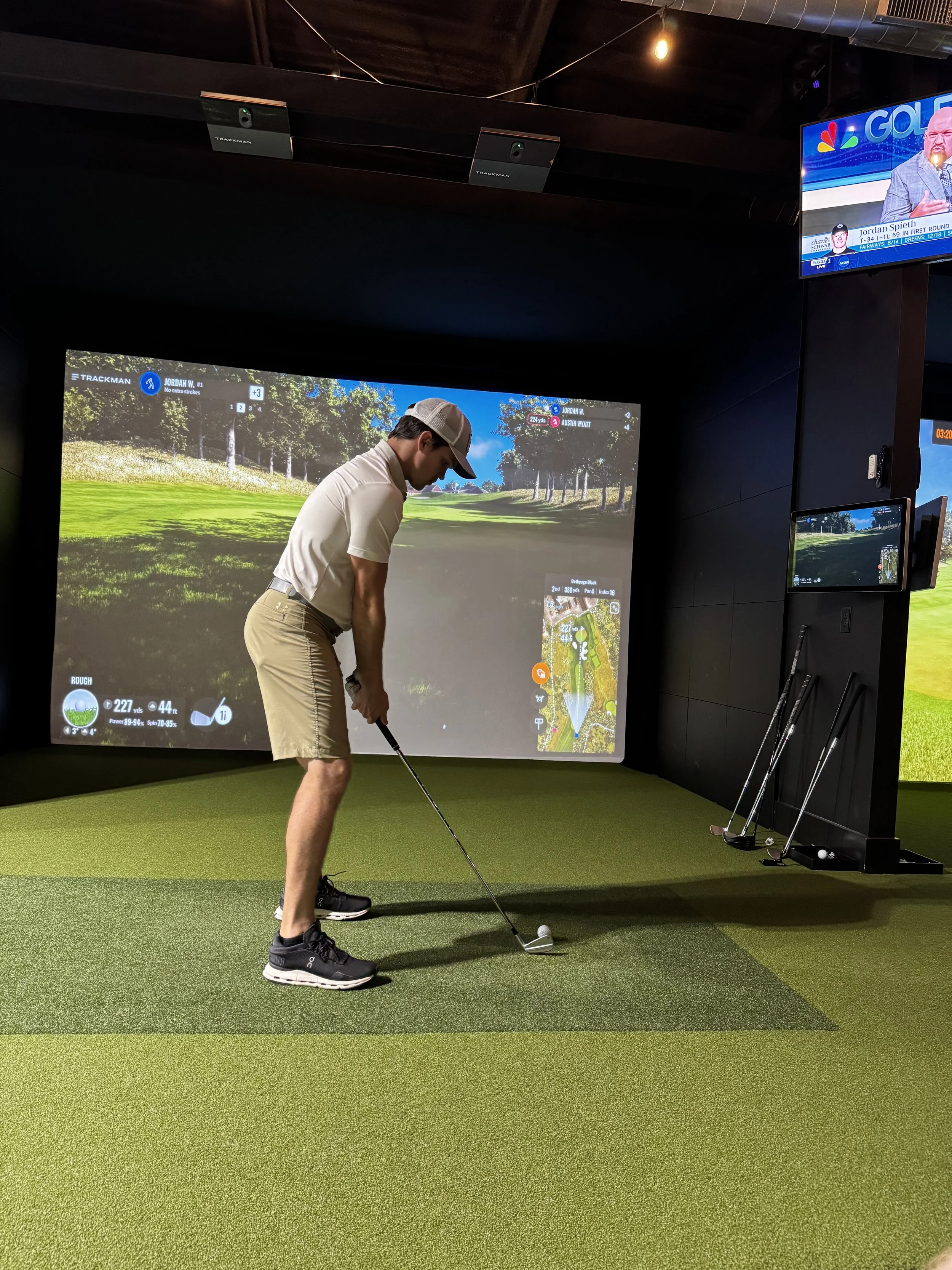 Golfer getting swings in on a TrackMan simulator at Broligans Indoor Golf, with live golf coverage playing on TV.