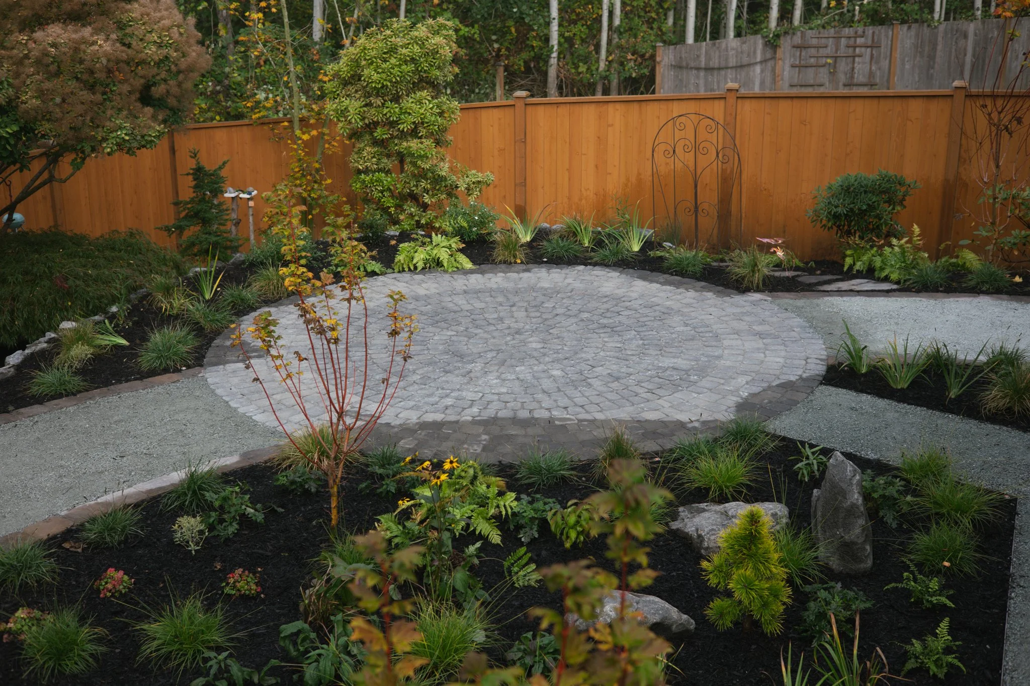 A circular cobblestone patio creates a welcoming gathering space, framed by gravel paths and layered planting.