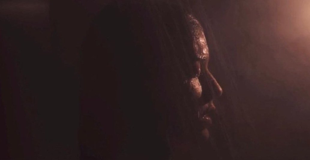 A dark image showing a close-up side profile of a person's face illuminated by a soft, warm light.