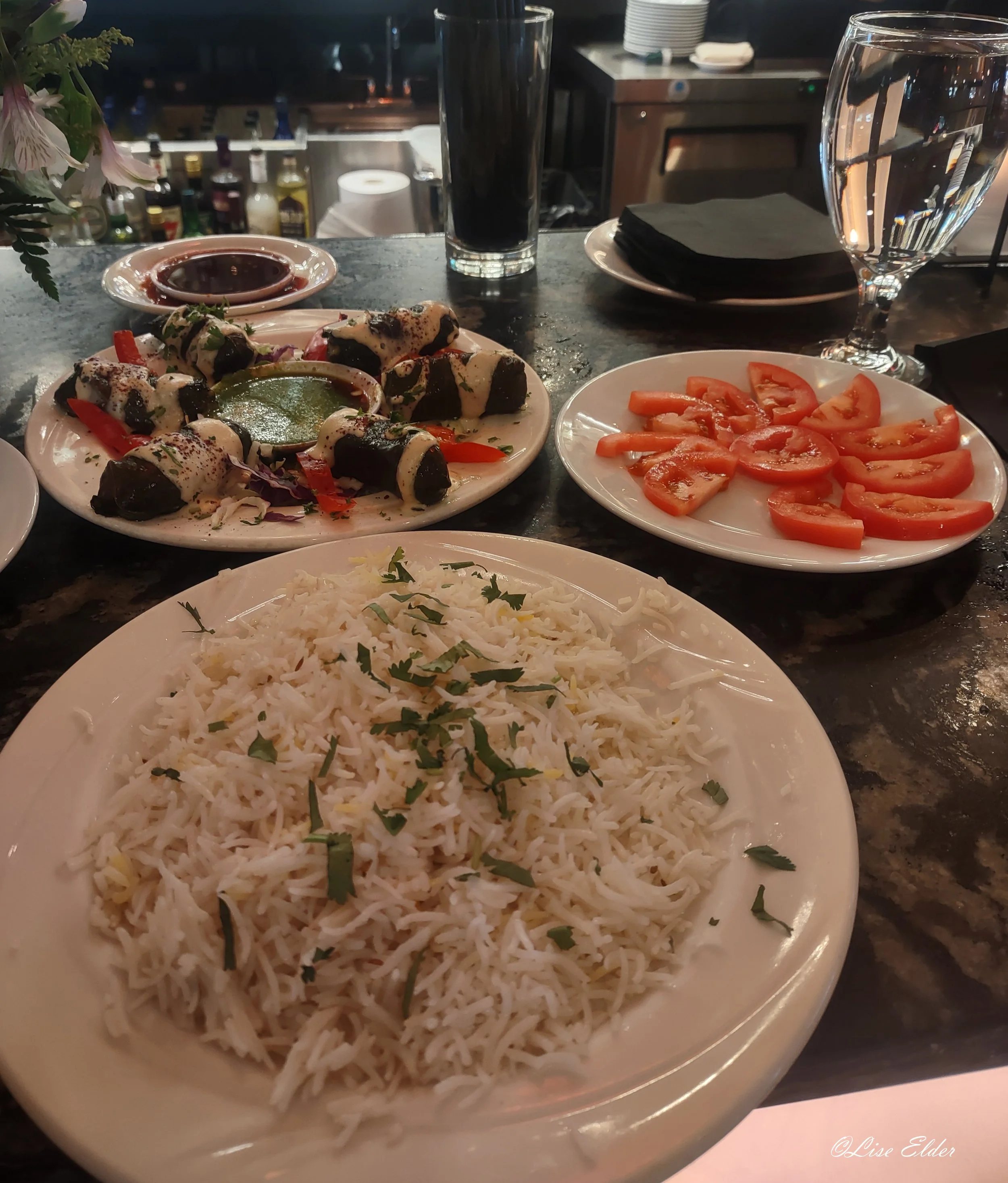 Indian food from a restaurant as an example of the wide variety of healthy choices in the real world. Saffron rice, stuffed grape leaves with tamarind and tahini, and a small plate of sliced tomatoes.