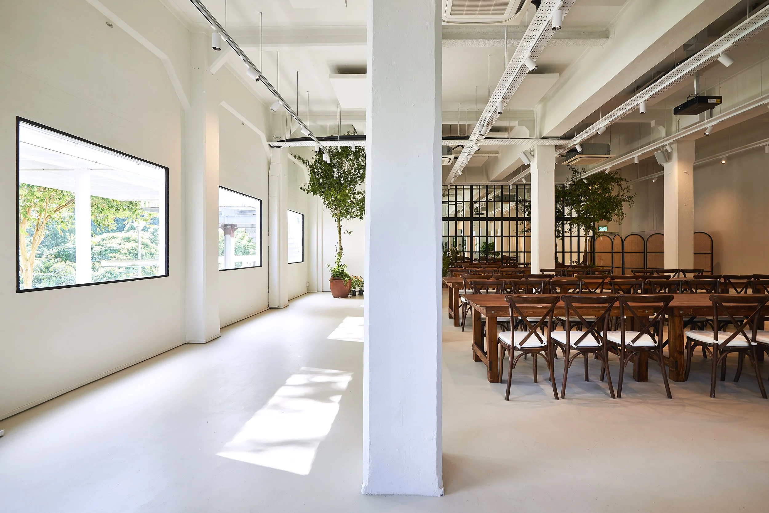 Interior Ida's Event Space in Gillman Barracks Singapore with high ceiling large windows, white walls, and wooden chairs and tables.